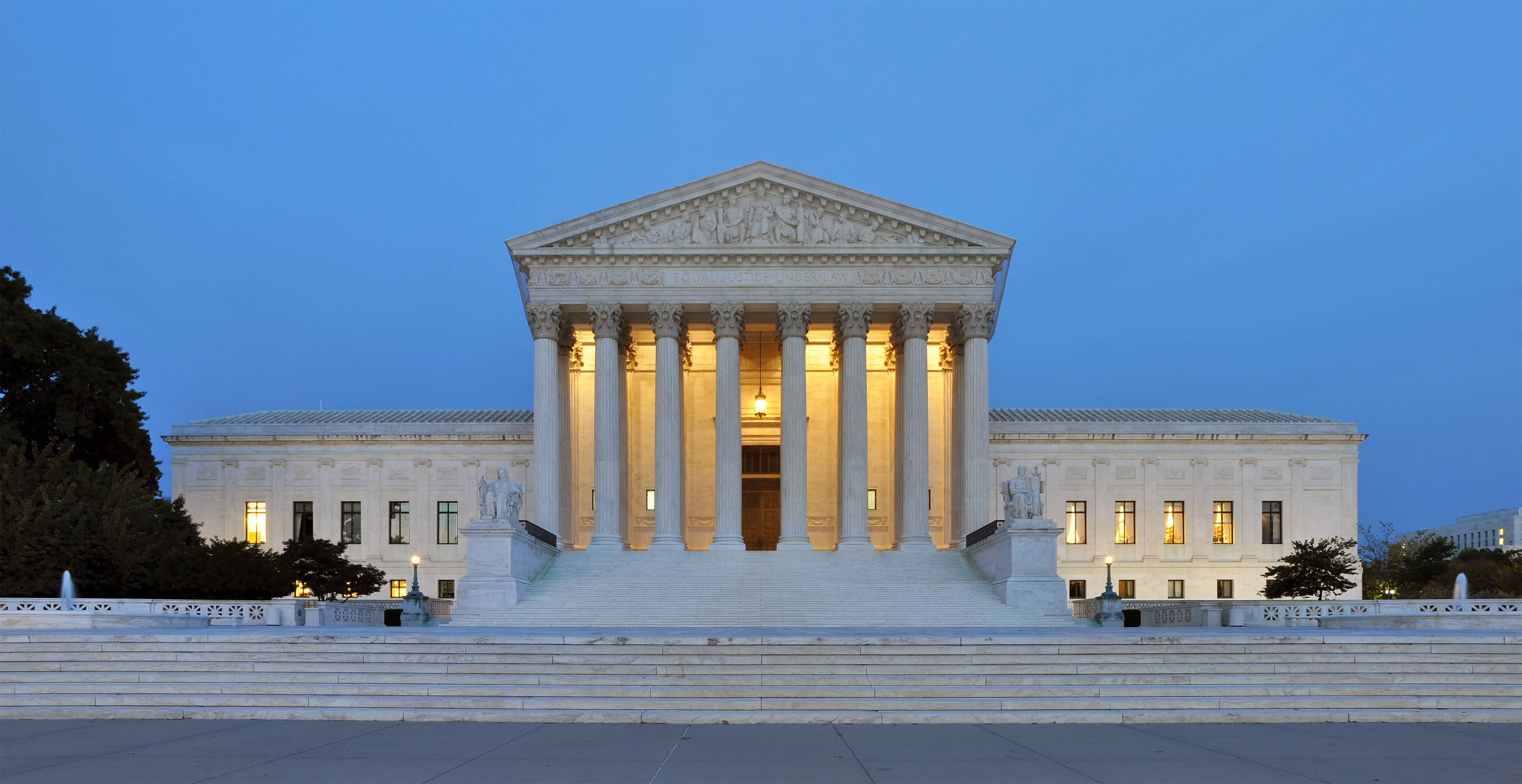 The illuminated U.S. Supreme Court Building facade at dusk with tall columns and marble steps.