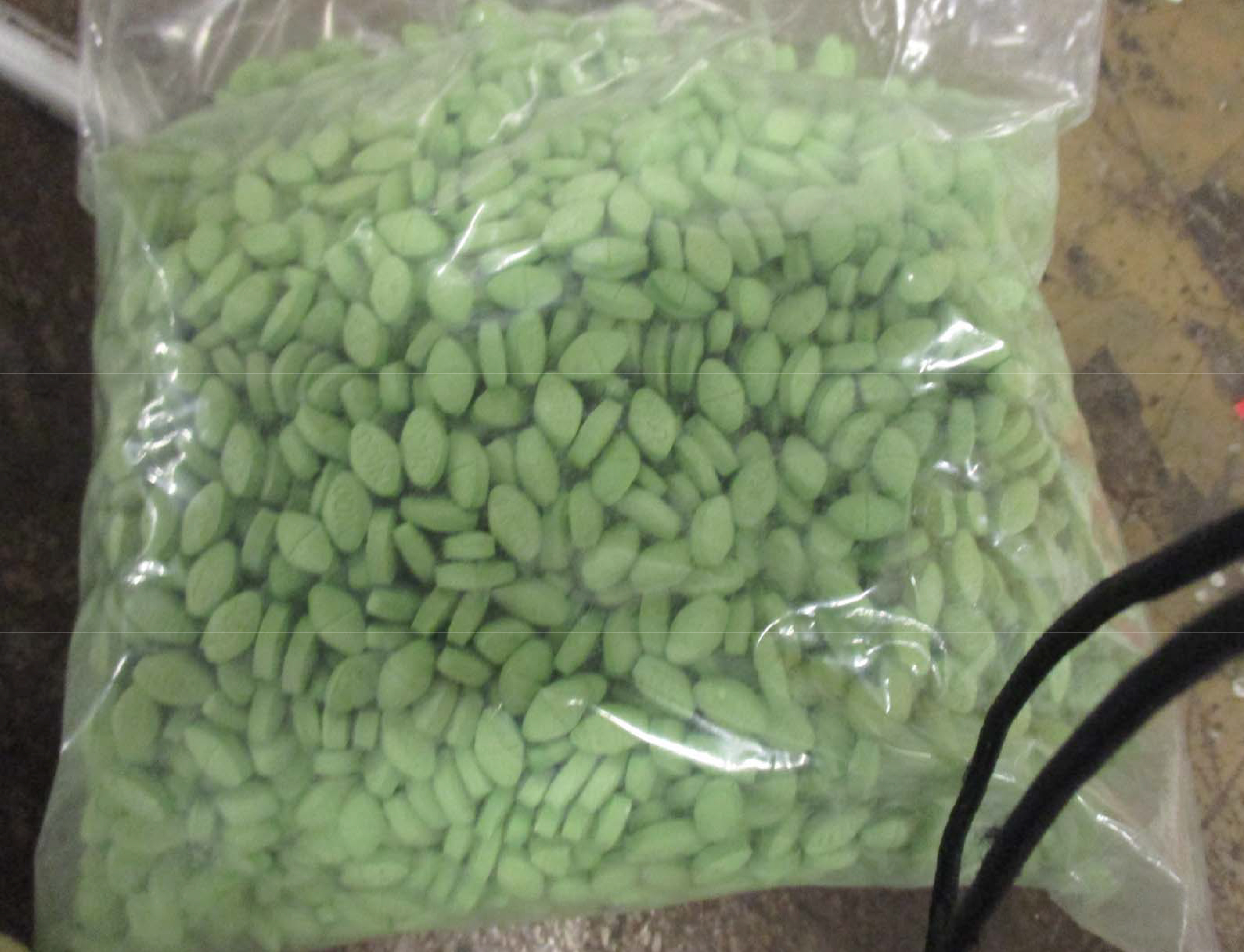 Clear plastic bag filled with hundreds of small, uniform green unlabeled pills.