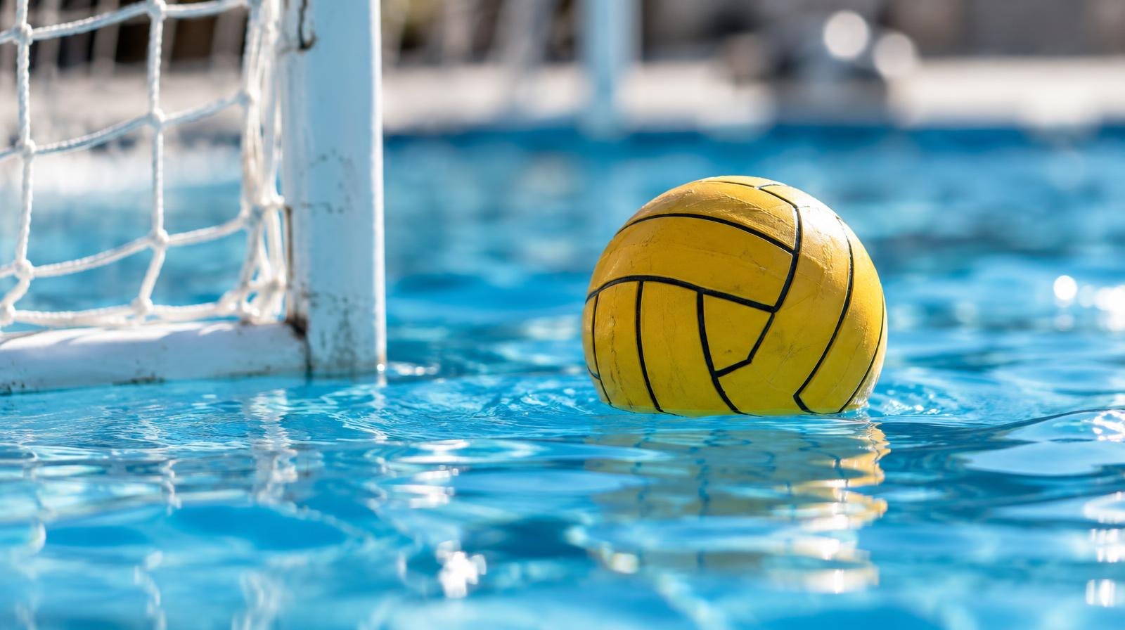 A water polo ball floating on the surface of a bright blue pool near a white goal net.