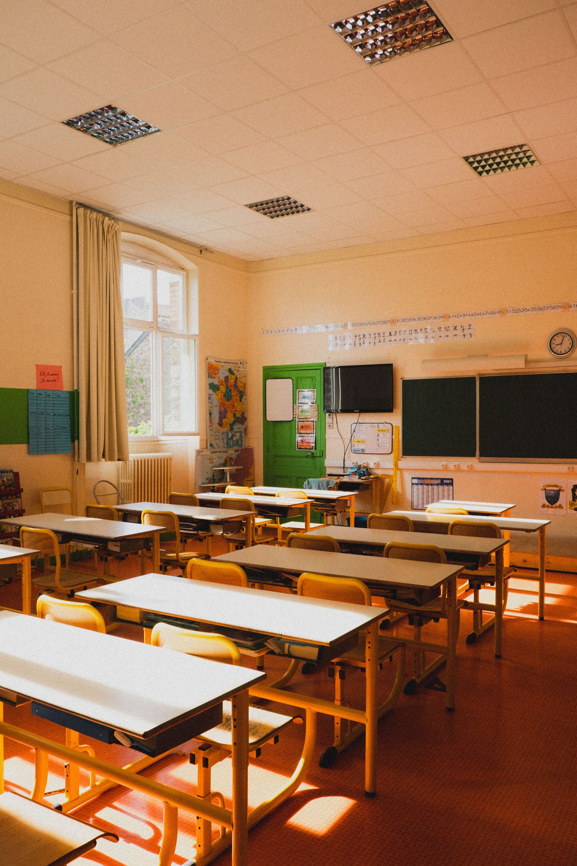 A bright, sunlit empty classroom with tables and chairs in Paris, France.