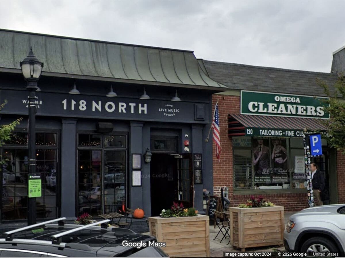 Two adjacent one-story storefronts, a bar and a dry cleaner, on a commercial block.