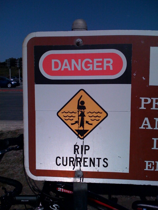 Red and white danger sign with swimmer warning symbol reading 'RIP CURRENTS'.