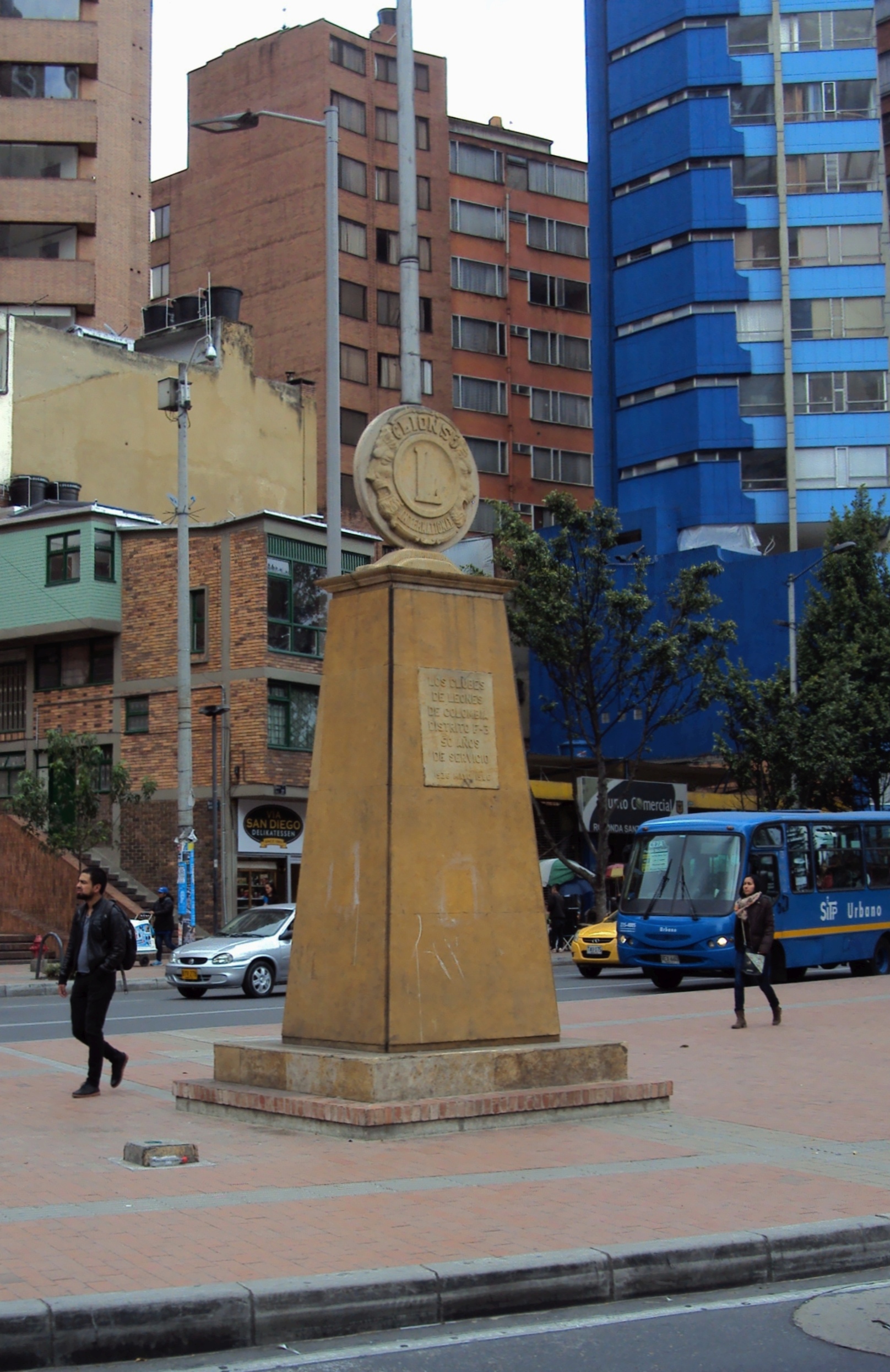 Tall stone obelisk monument topped with the Lions International emblem in an urban plaza.