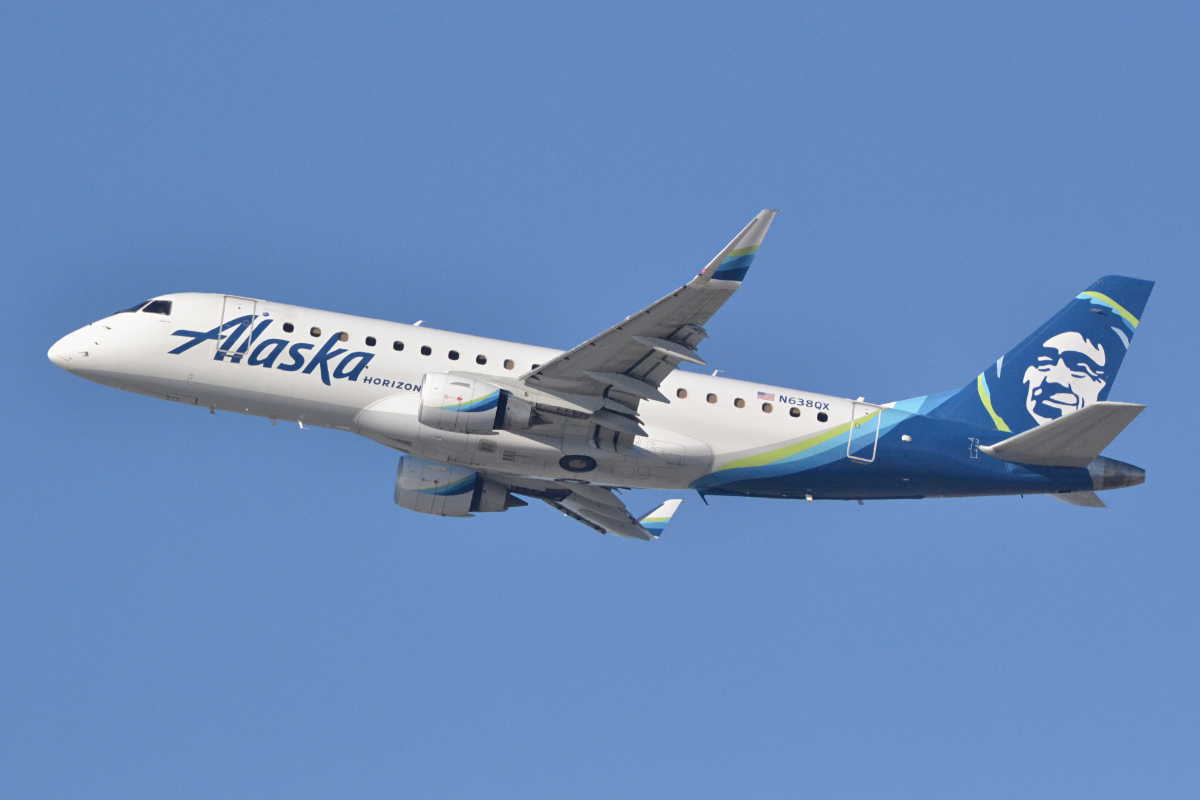 Alaska Airlines Horizon Air Embraer E175 jet in flight against a clear blue sky.