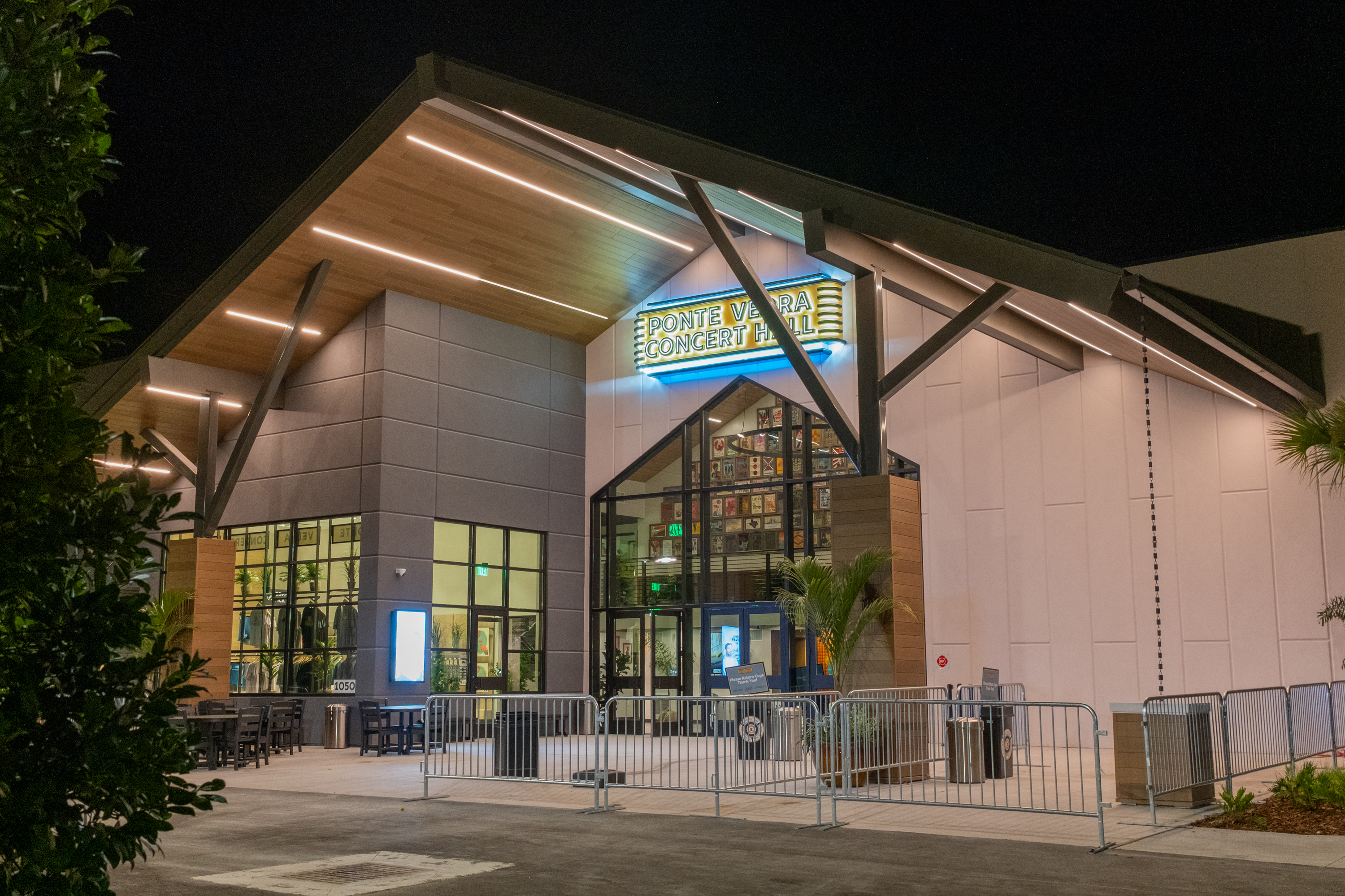Illuminated exterior of a modern concert hall at night with crowd barriers at the entrance.