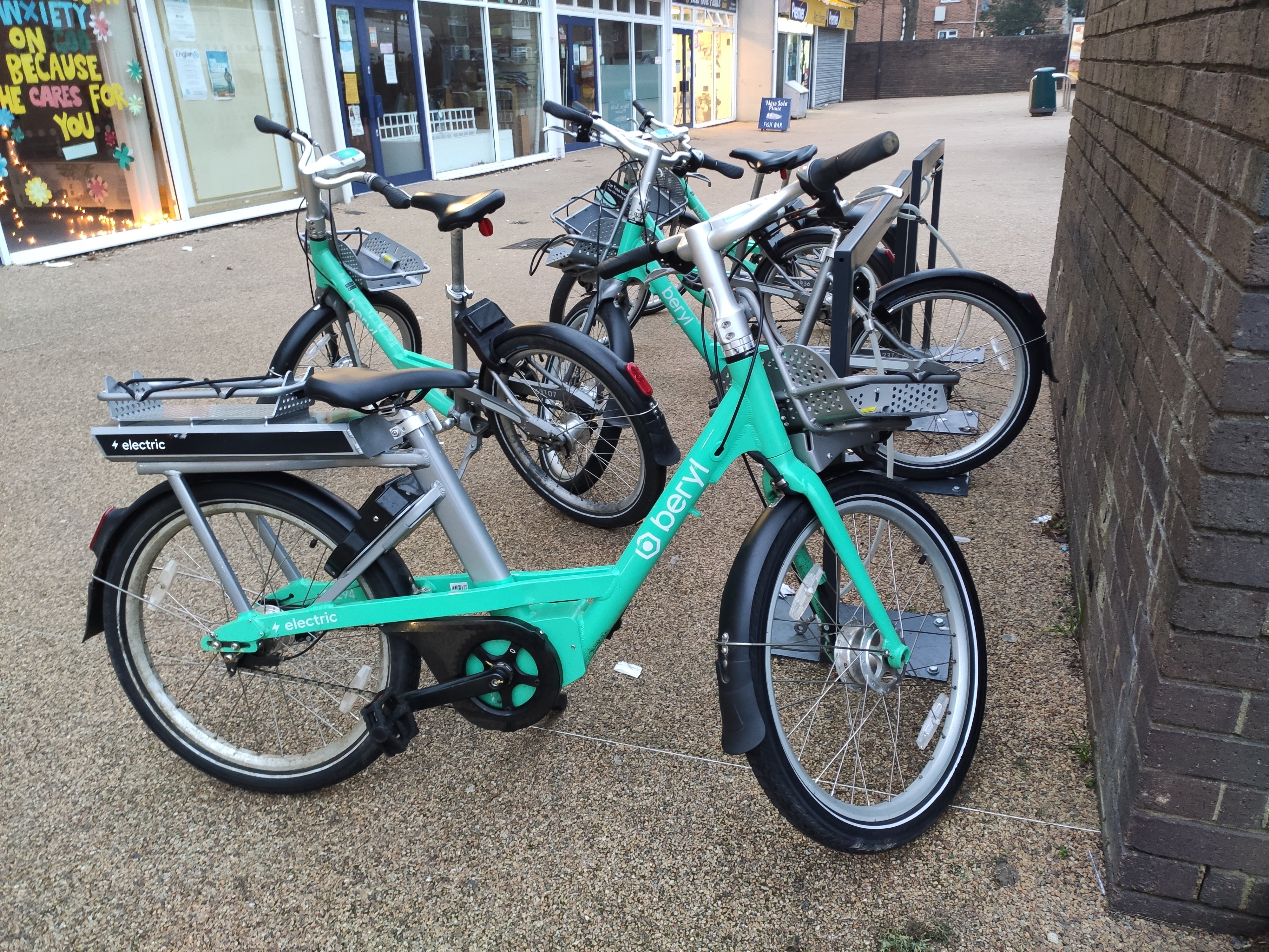 Several teal electric bikes parked together on a sidewalk near storefronts.