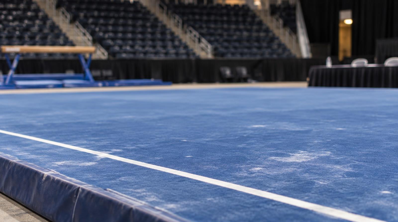 An empty gymnastics floor exercise mat with colored boundary lines under bright arena lights.