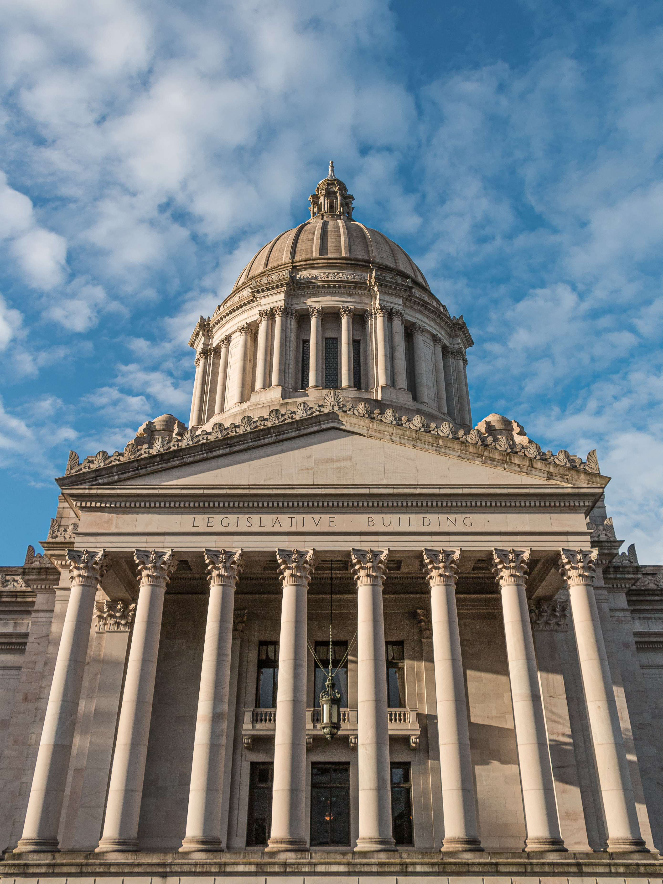 Neoclassical government building with large dome and tall columns under a blue sky.