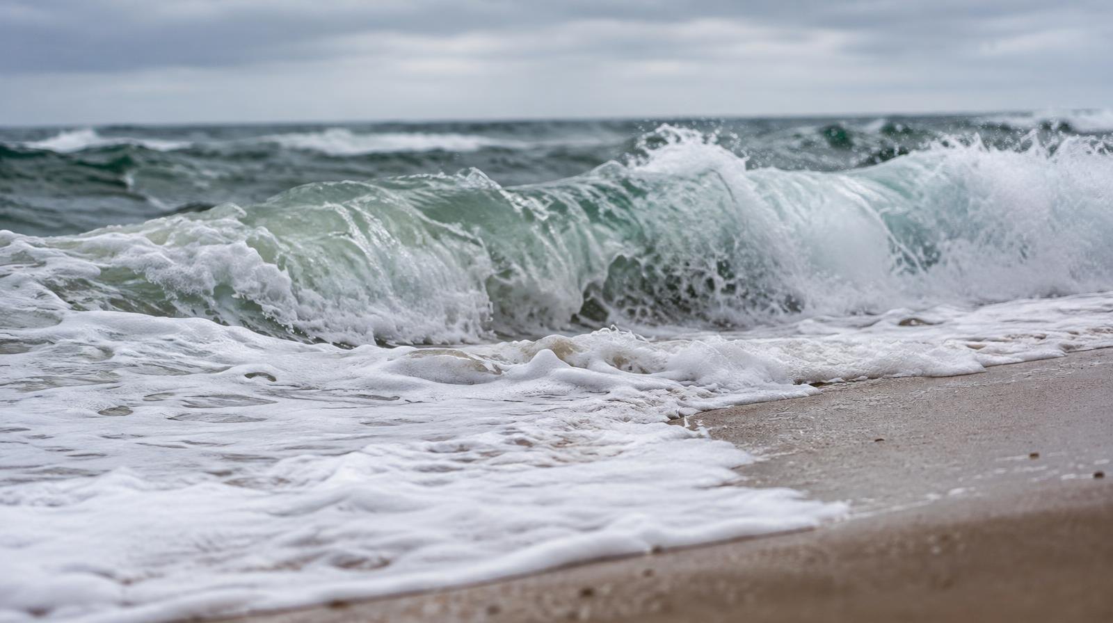 Large ocean waves breaking on a sandy beach with white foam rushing up the shore.