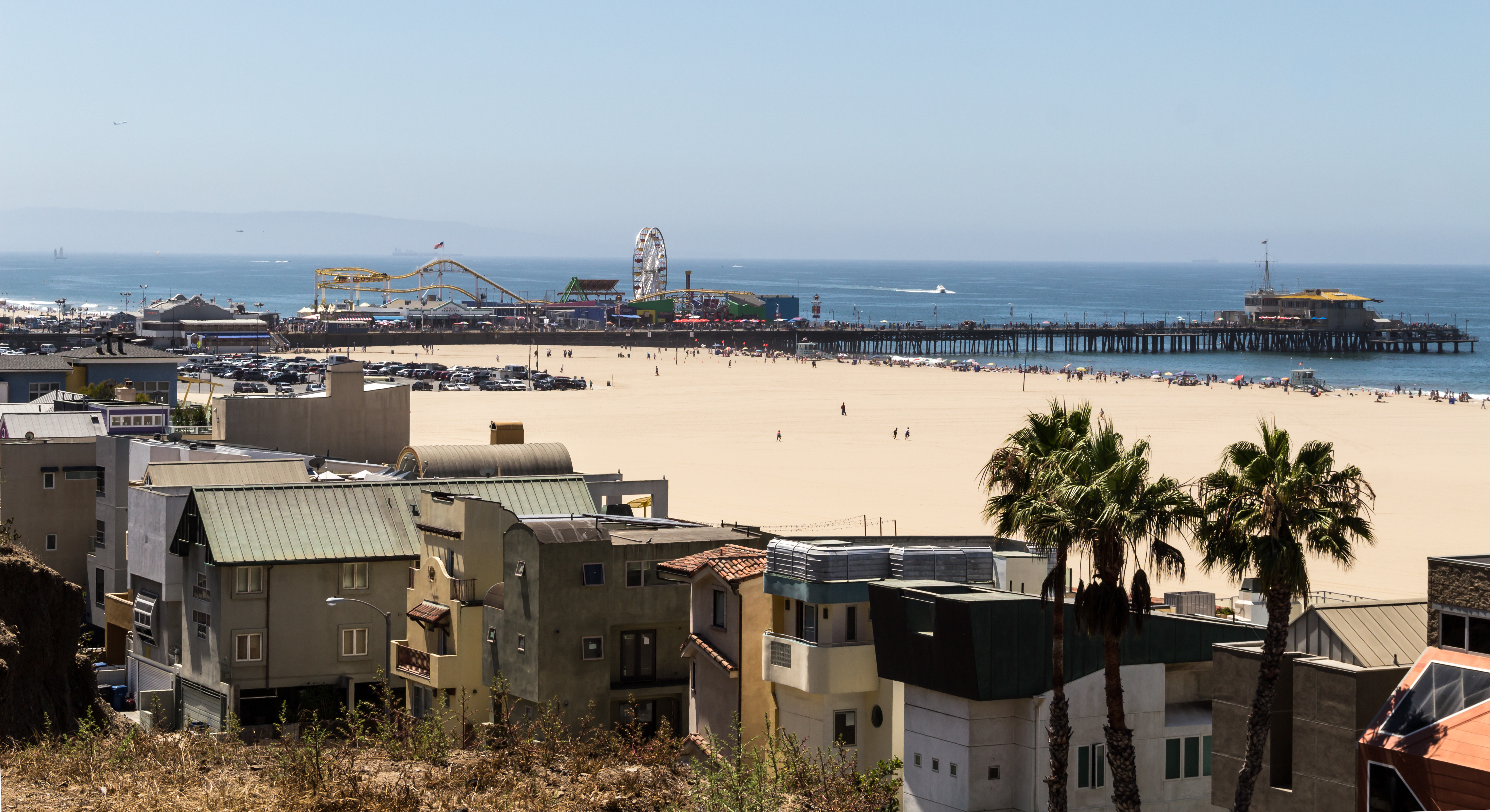Aerial view of a sandy beach with a pier, Ferris wheel, and beachfront buildings.