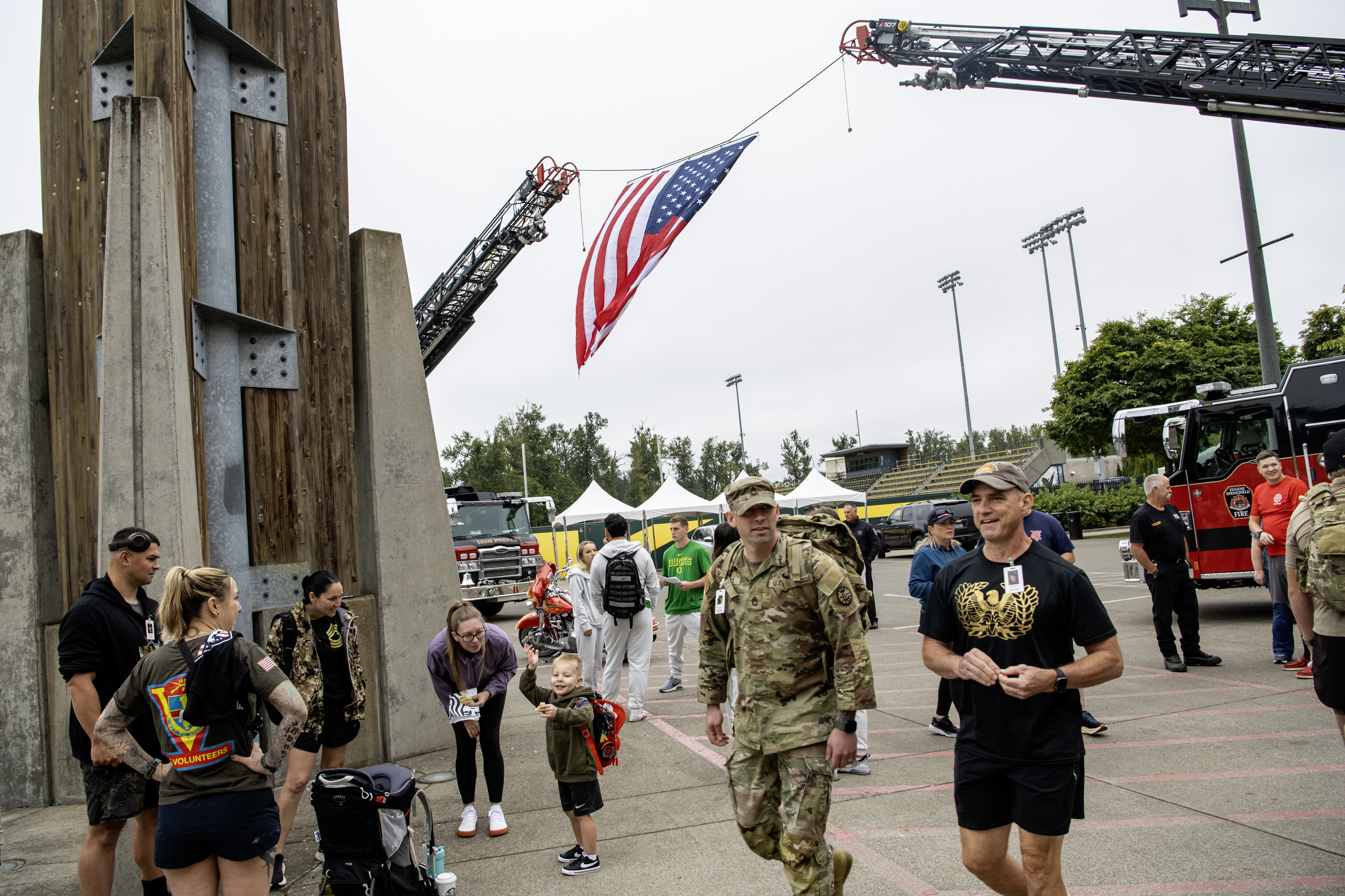 American flag suspended between two fire truck ladders at an outdoor 9/11 memorial event.