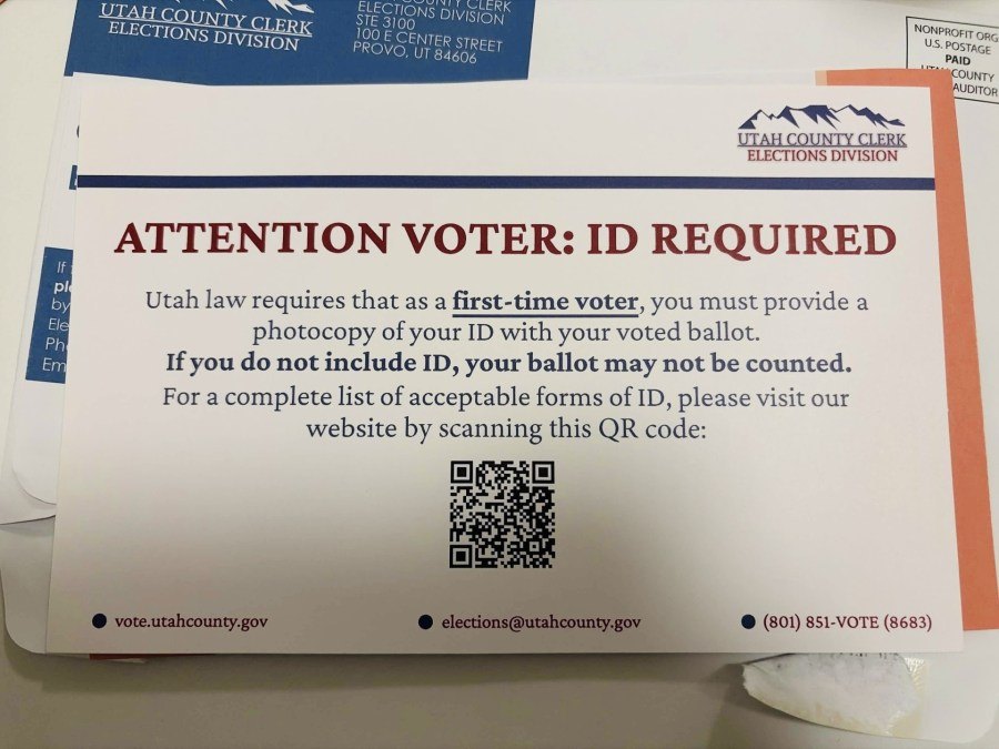 Printed card reading 'Attention Voter: ID Required' with instructions and a QR code.