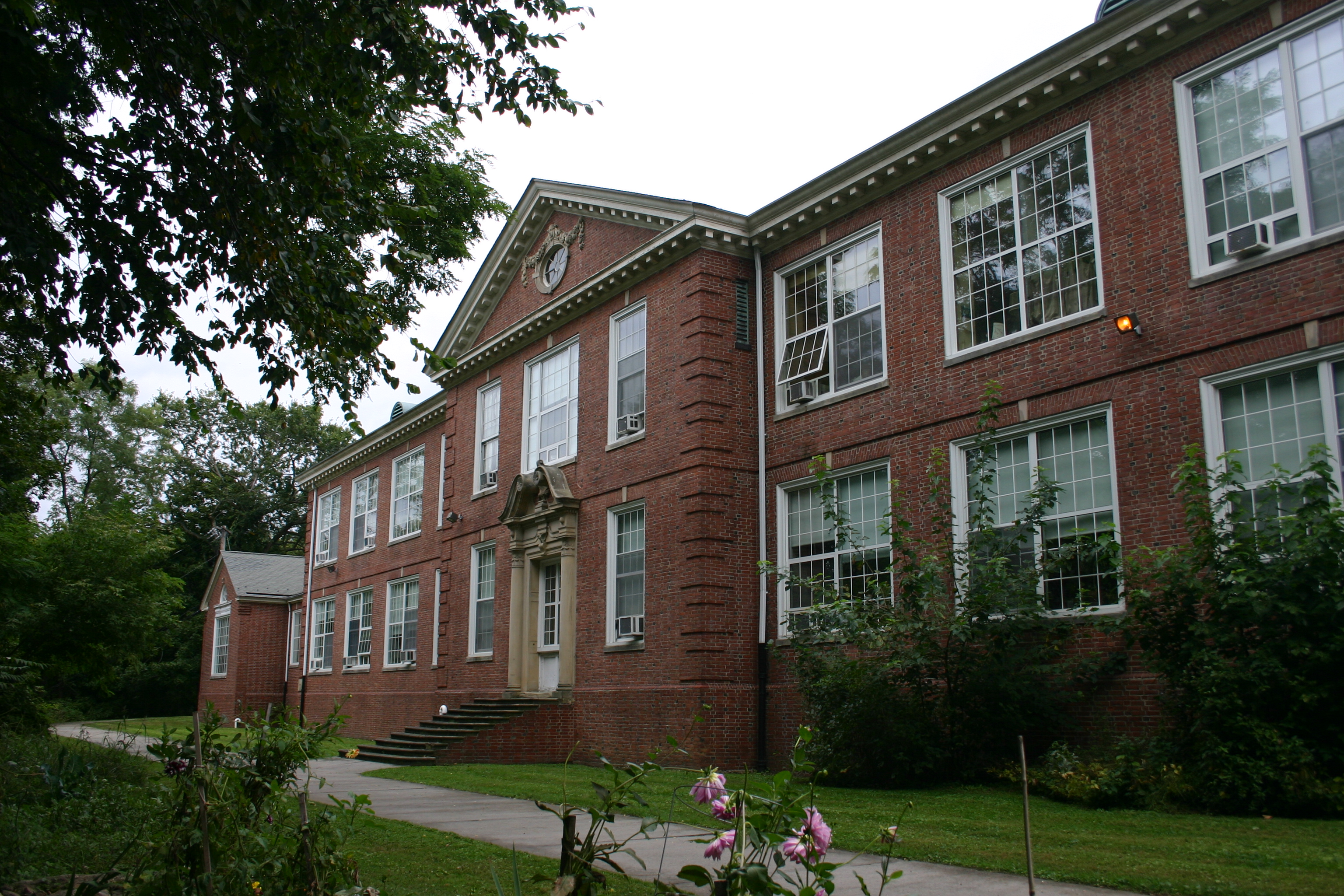 Red brick multi-story school building with white-trimmed windows and landscaping.