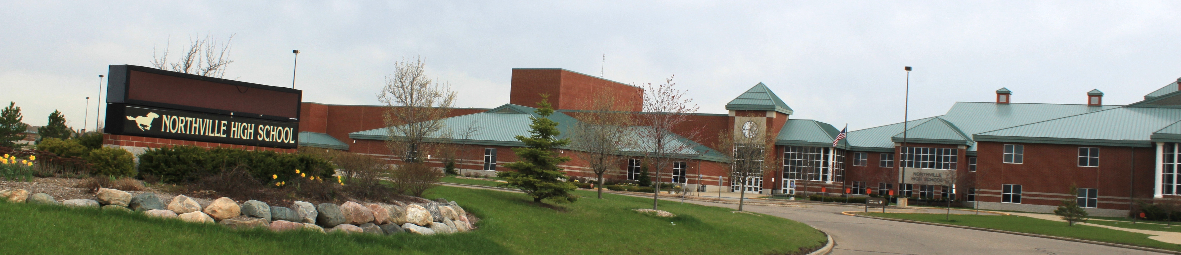 Exterior view of a brick high school building with entrance sign and green roof accents.