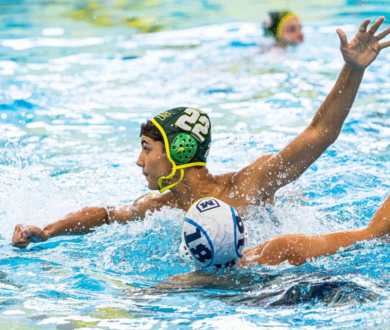 Water polo player in a green numbered cap reaches for a ball in a pool.