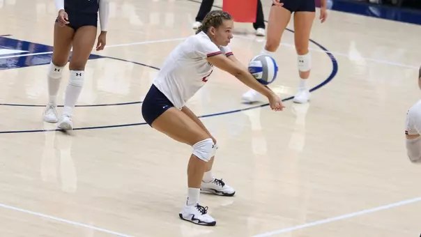 Female volleyball player in white jersey lunges low in a defensive dig stance.