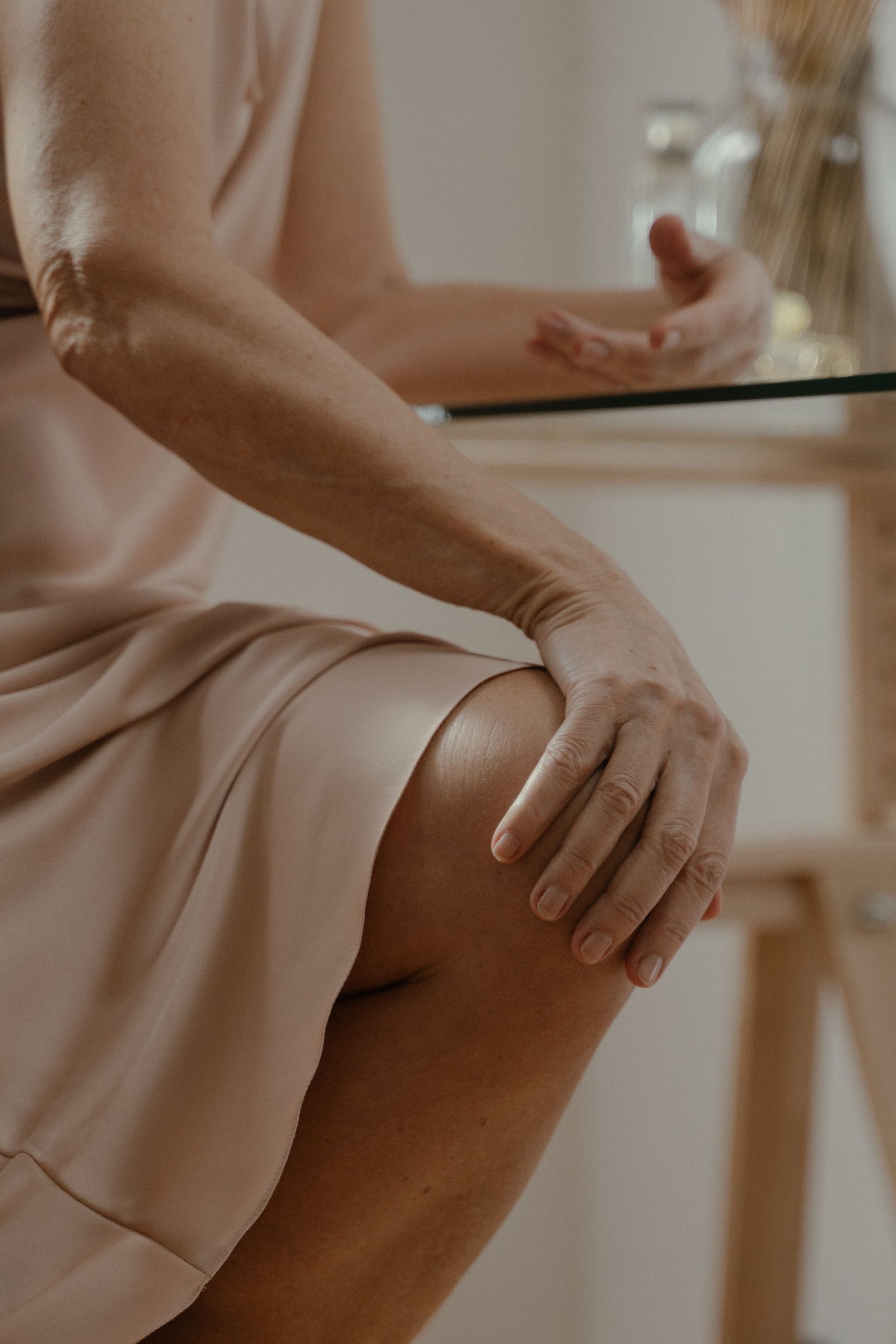An artistic close-up of a woman's hand resting on her knee indoors.