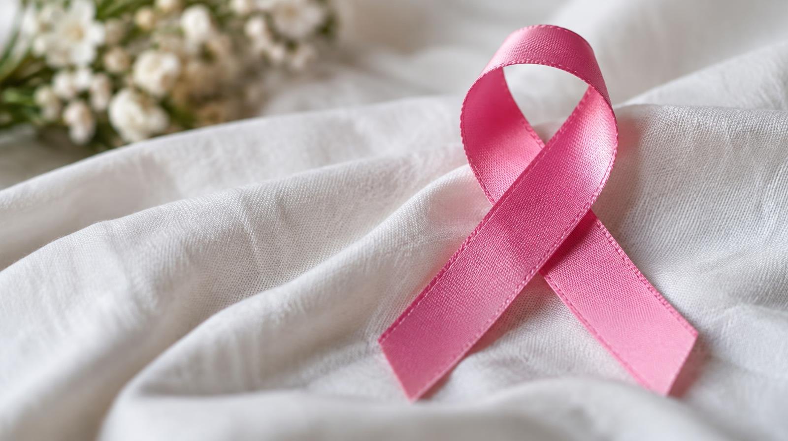 A pink ribbon resting on a soft white fabric surface.