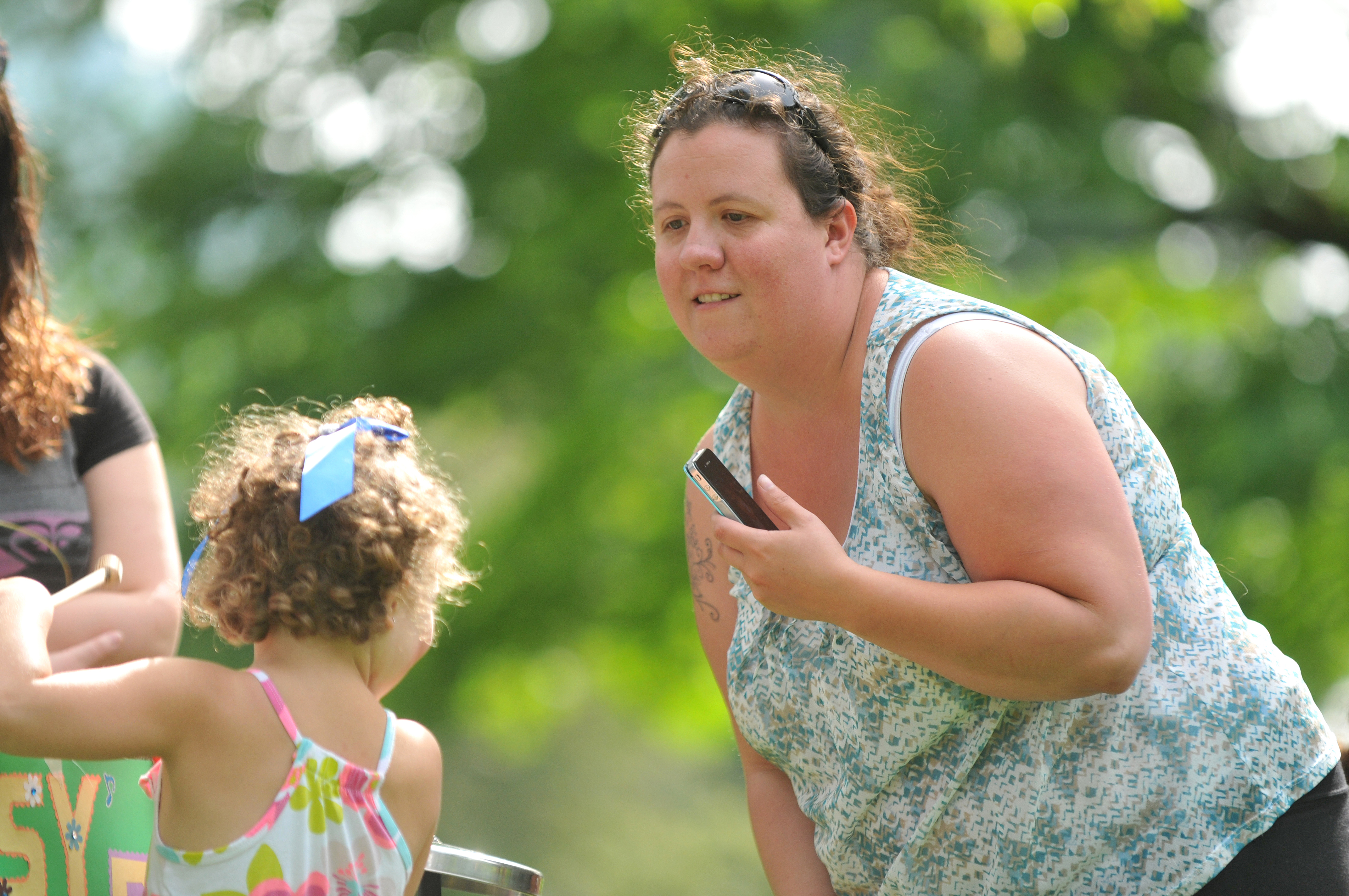 A woman leans toward a young curly-haired child outdoors at a community gathering.