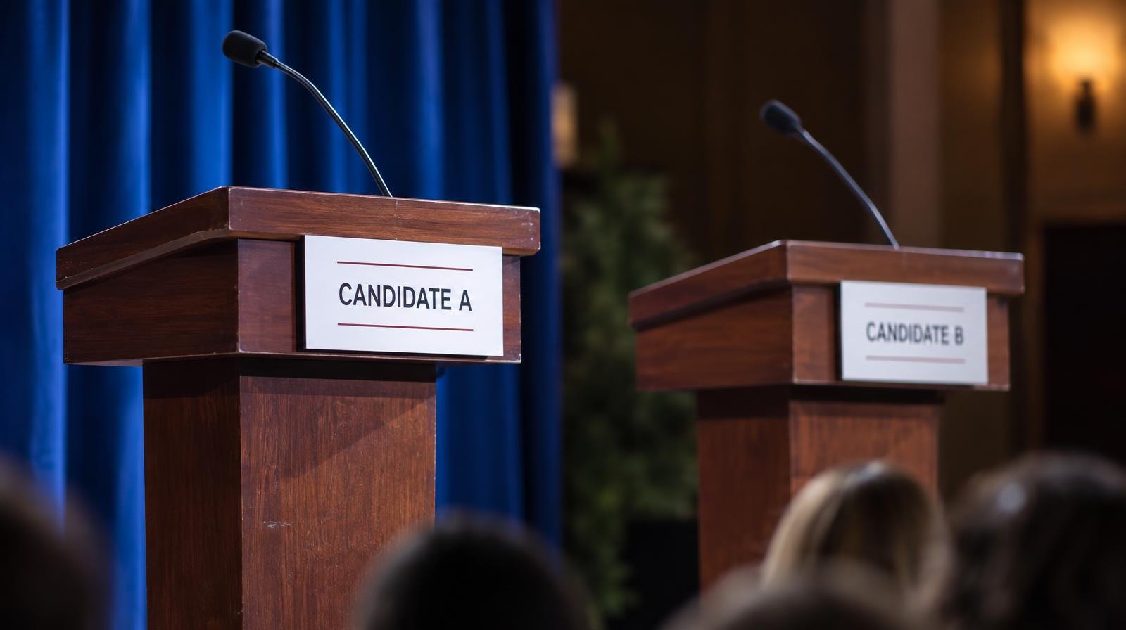 Two empty podiums with microphones on a lit stage in an auditorium.