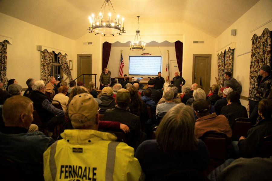 Crowded indoor meeting hall with rows of seated attendees facing a presentation screen.