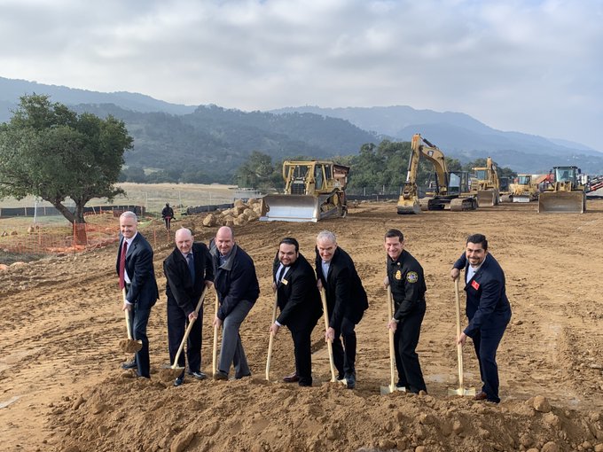 Officials holding golden shovels at a fire station groundbreaking ceremony on a cleared dirt lot.