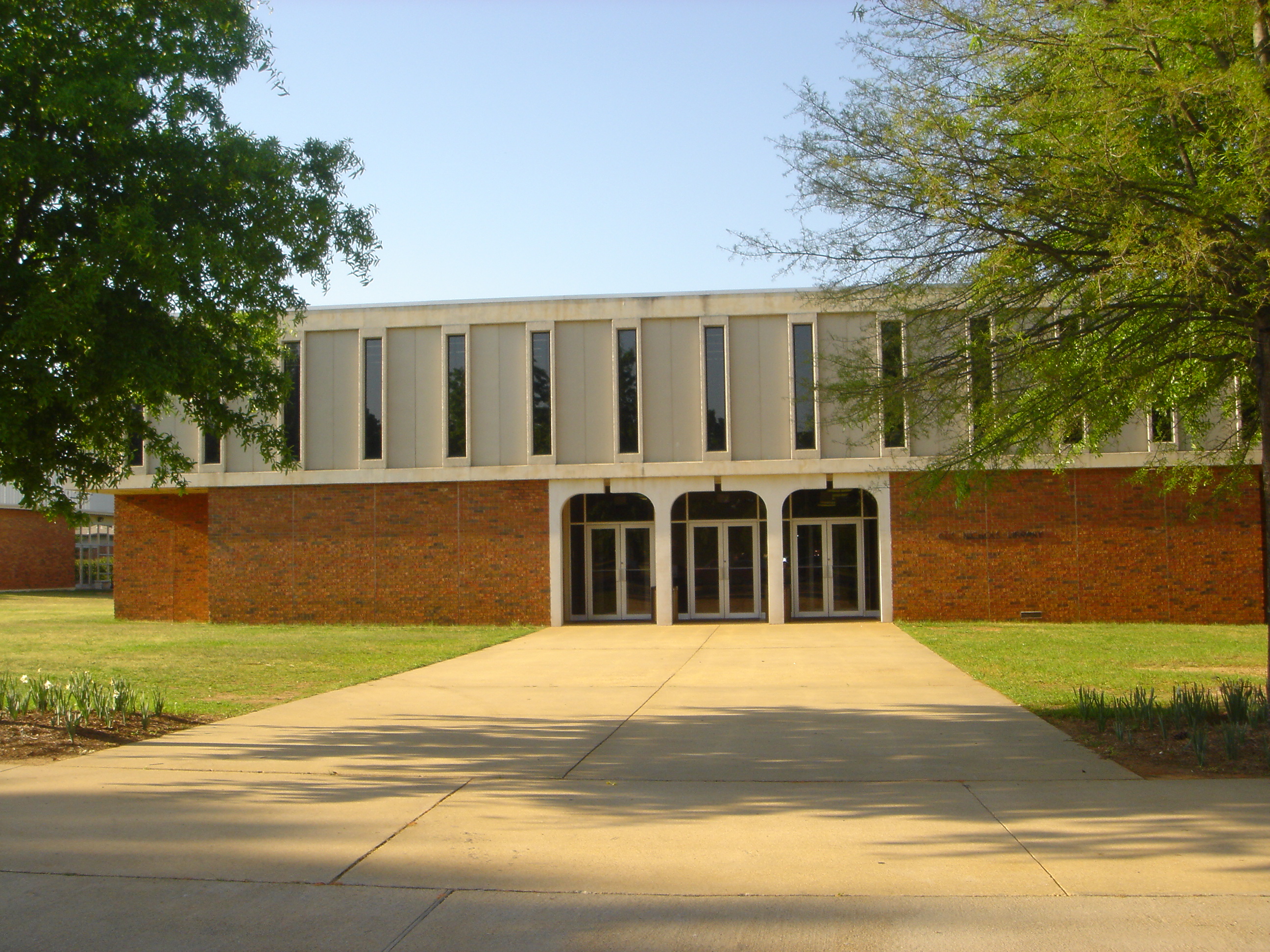 Two-story brick and glass library building with arched entrance and concrete walkway.