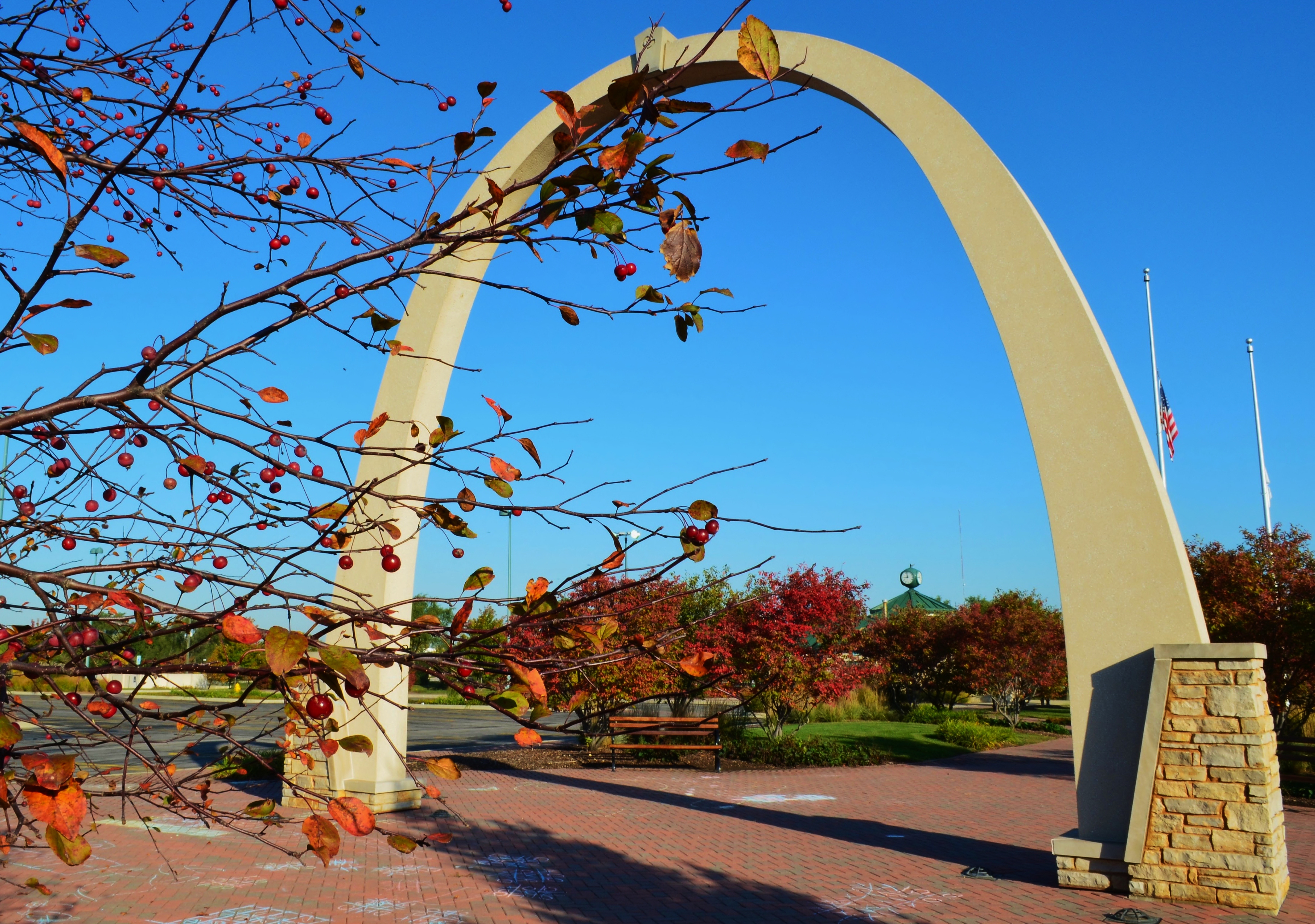 Concrete arch over a brick walkway surrounded by autumn trees with red berries.
