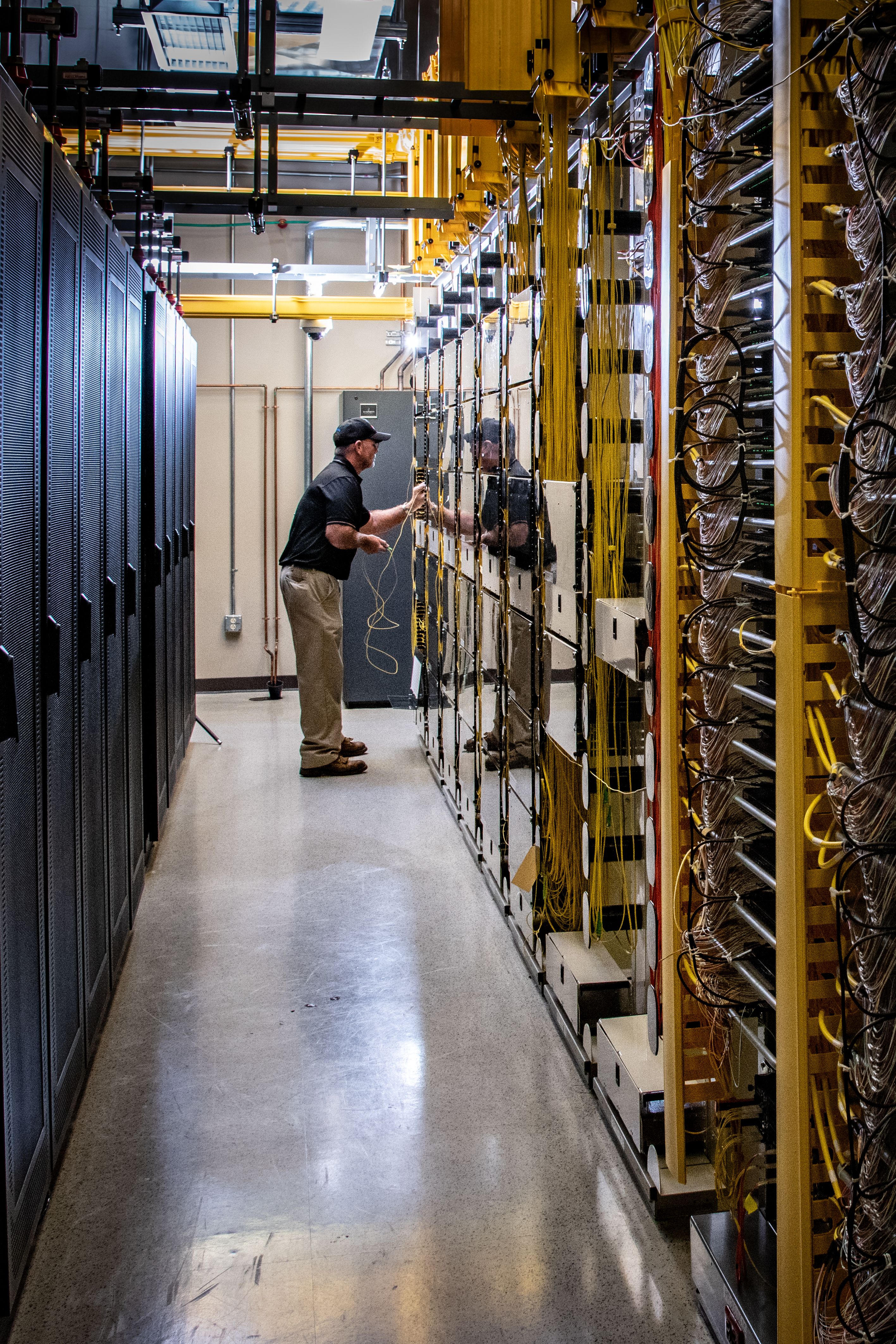 Technician walking through a data center aisle lined with tall yellow server racks.
