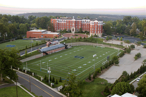 Aerial view of a school campus with a football field, bleachers, and a large brick building.