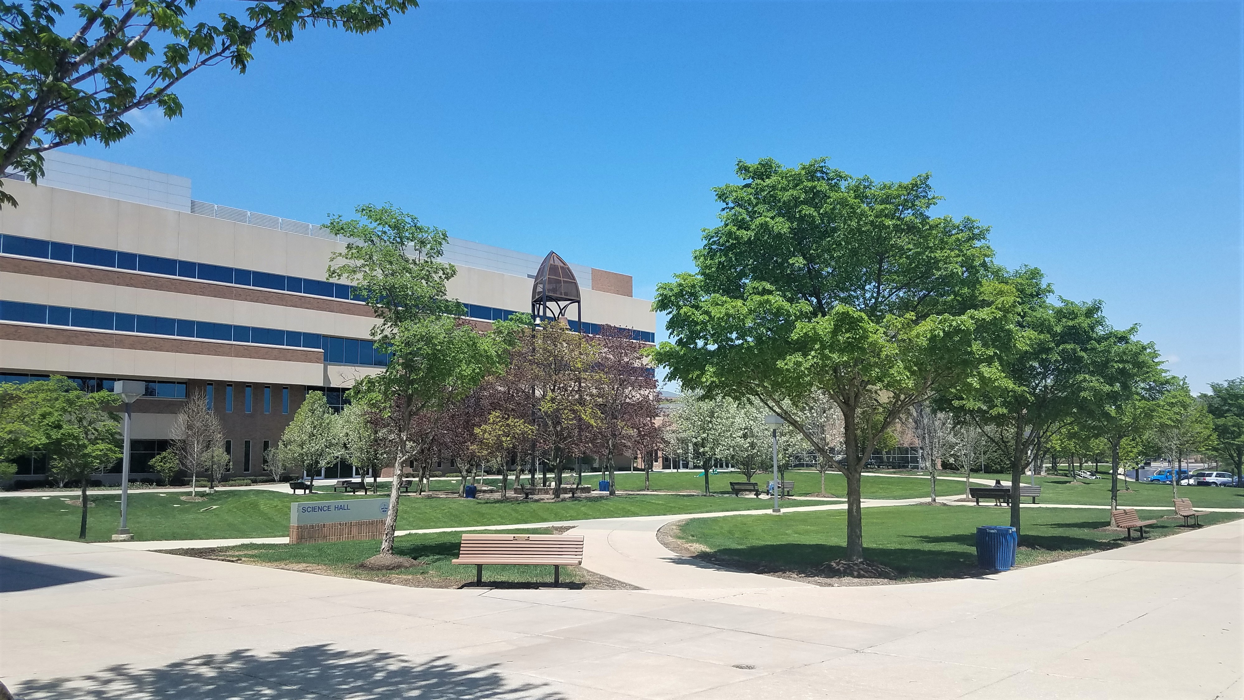 A multi-story academic building with a bell tower surrounded by green lawns and trees on a university campus.