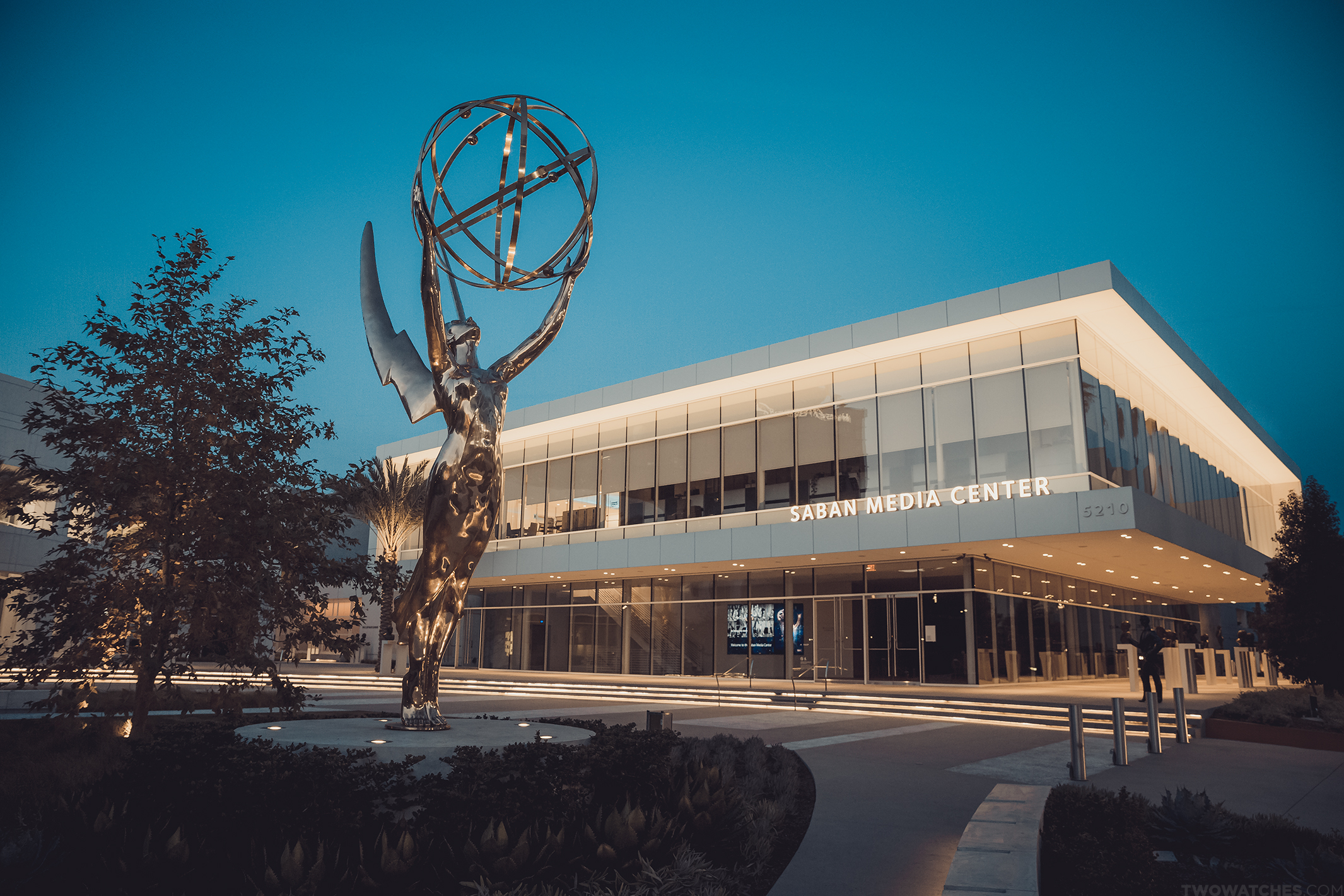 Emmy Award statue stands before the Saban Media Center building at dusk.
