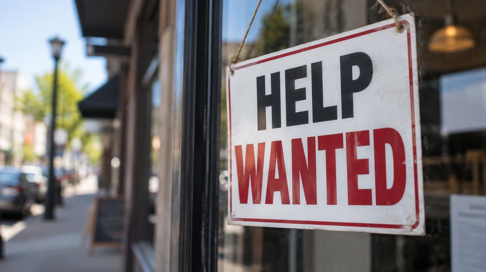 A Help Wanted sign hanging in a storefront window.