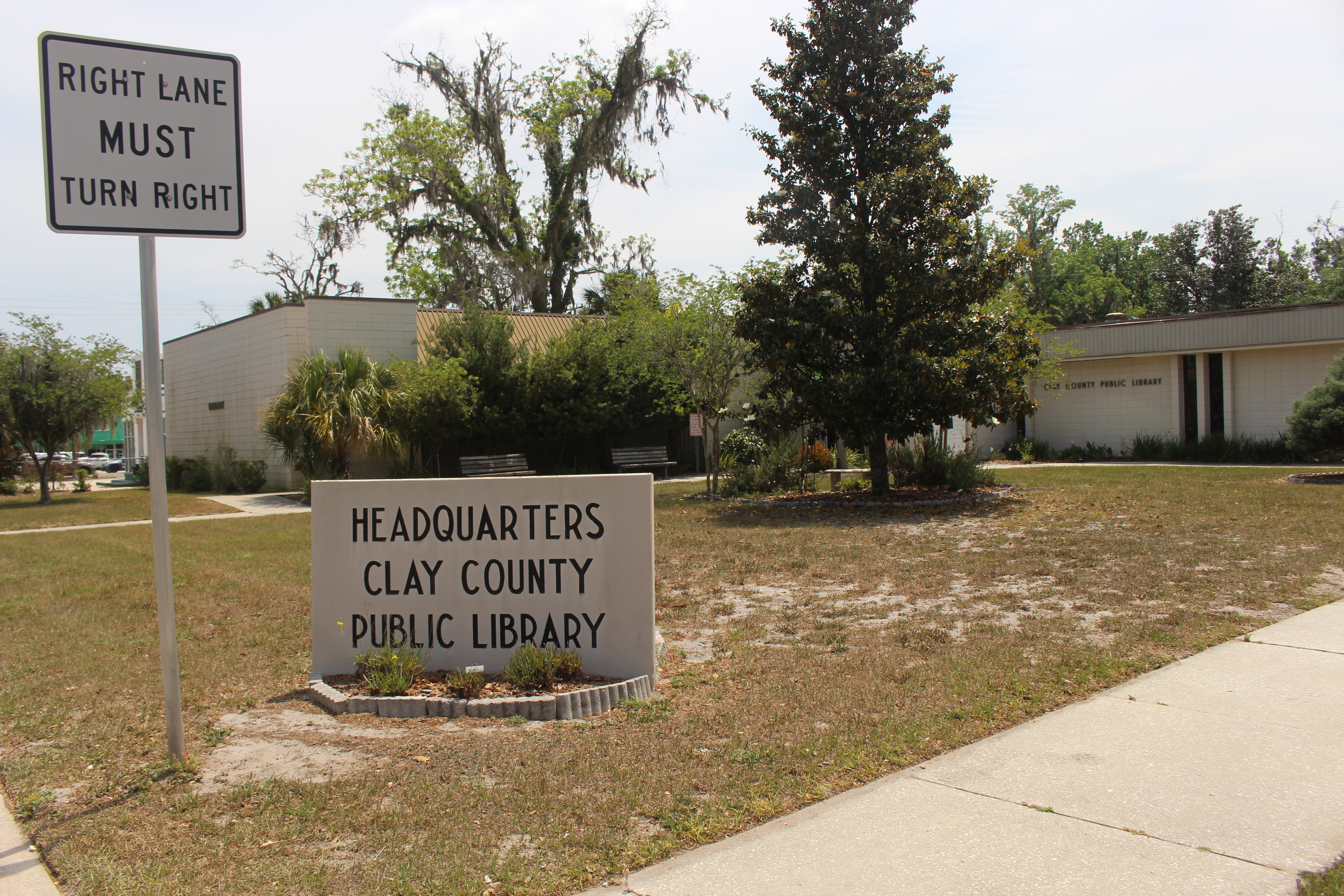 Low single-story library building with a stone sign reading Headquarters Clay County Public Library.