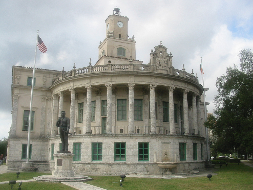 Neoclassical city hall with curved colonnade, clock tower, and bronze statue on the grounds.