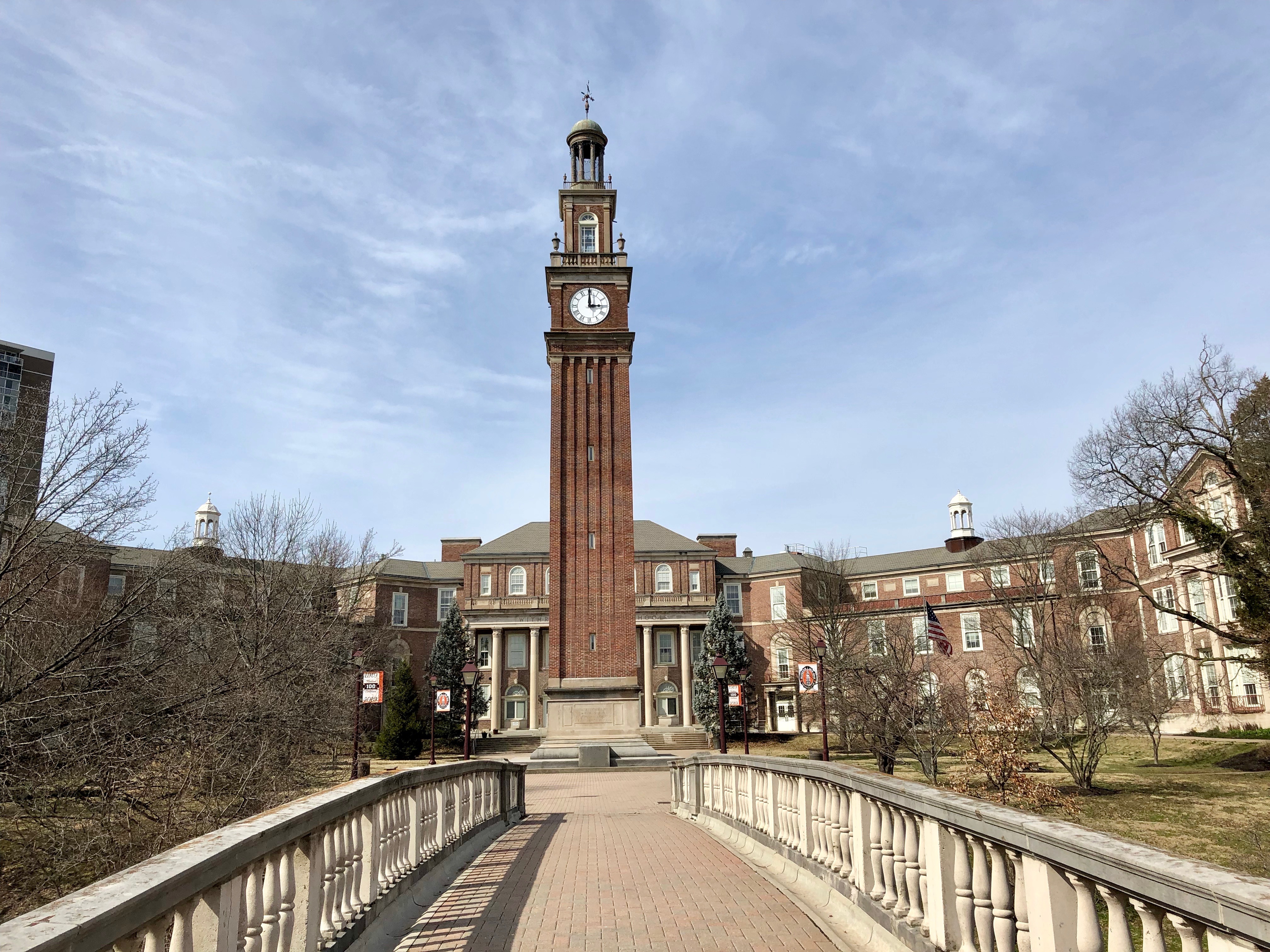 Brick clock tower and stone walkway at the entrance of a large school building.