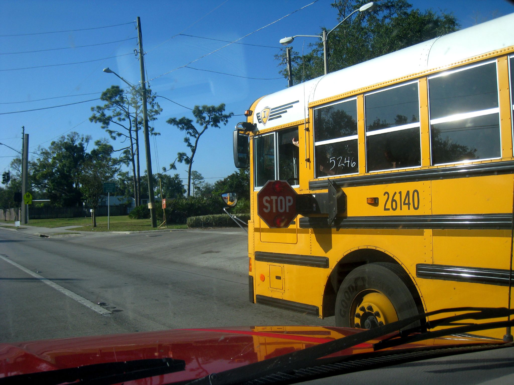 Yellow school bus with red stop arm extended, seen from a following vehicle.