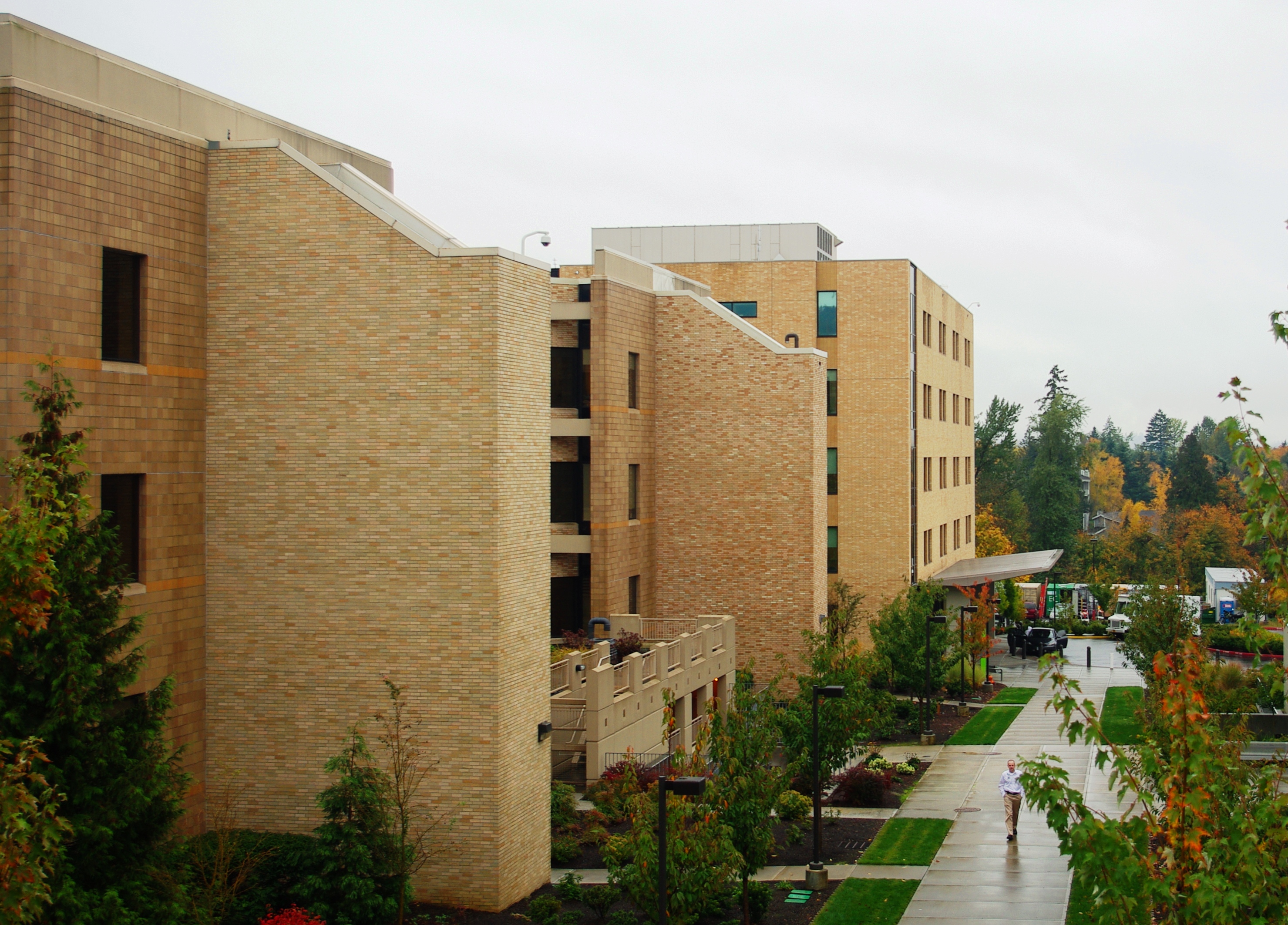 Multi-story tan brick medical center building with landscaped walkways on an overcast day.