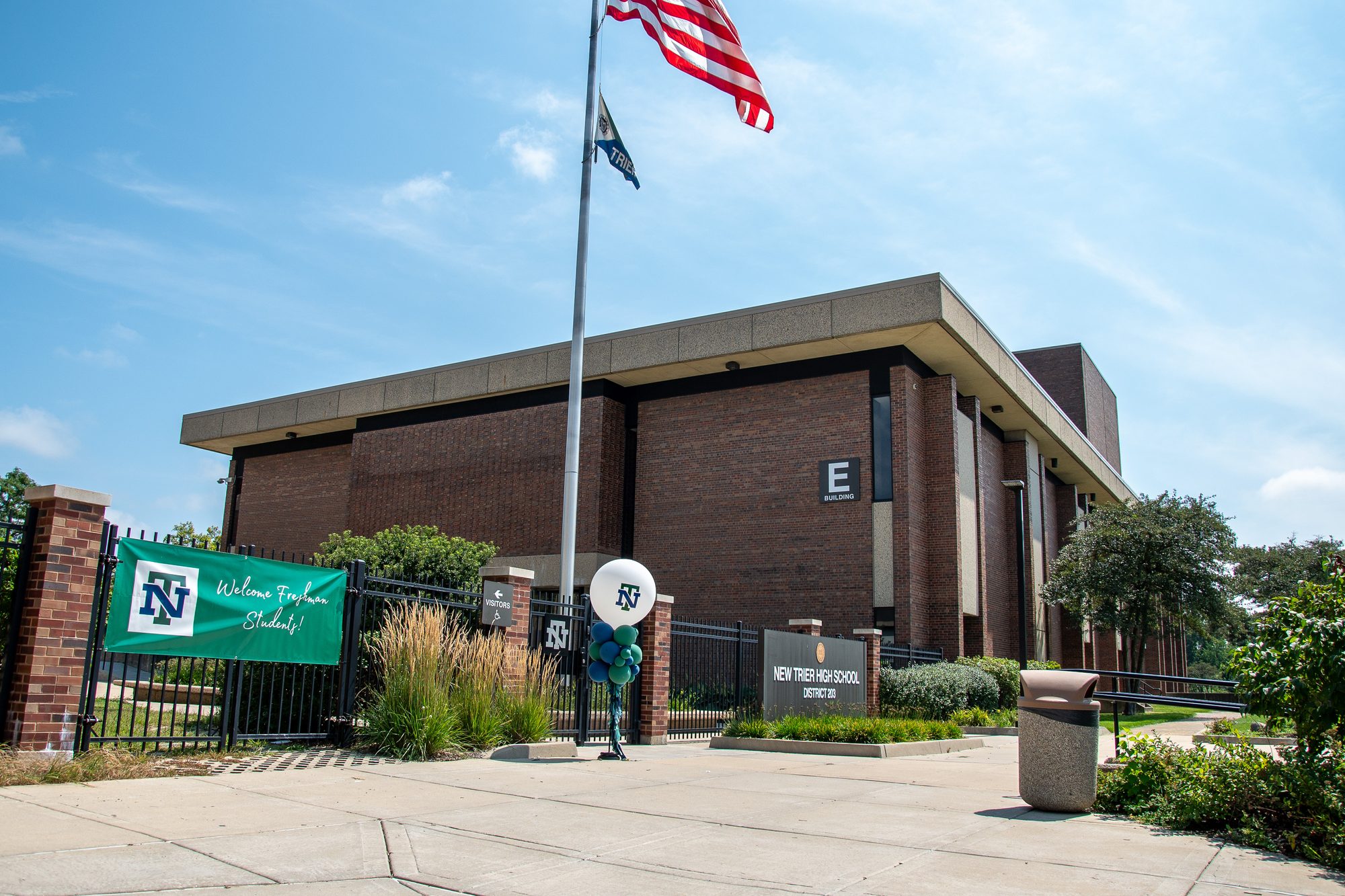 Brick high school building entrance with an American flag and a green welcome banner.