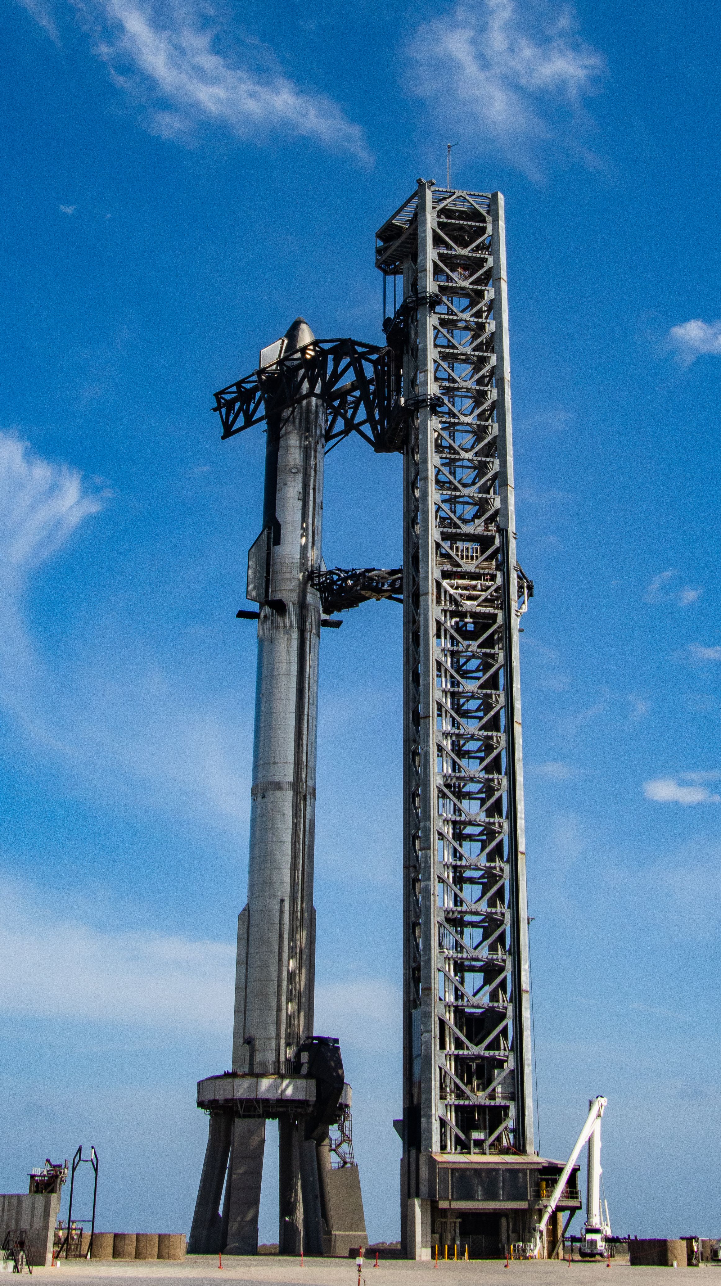 Tall stainless-steel rocket stack on a launch mount beside a towering steel structure.
