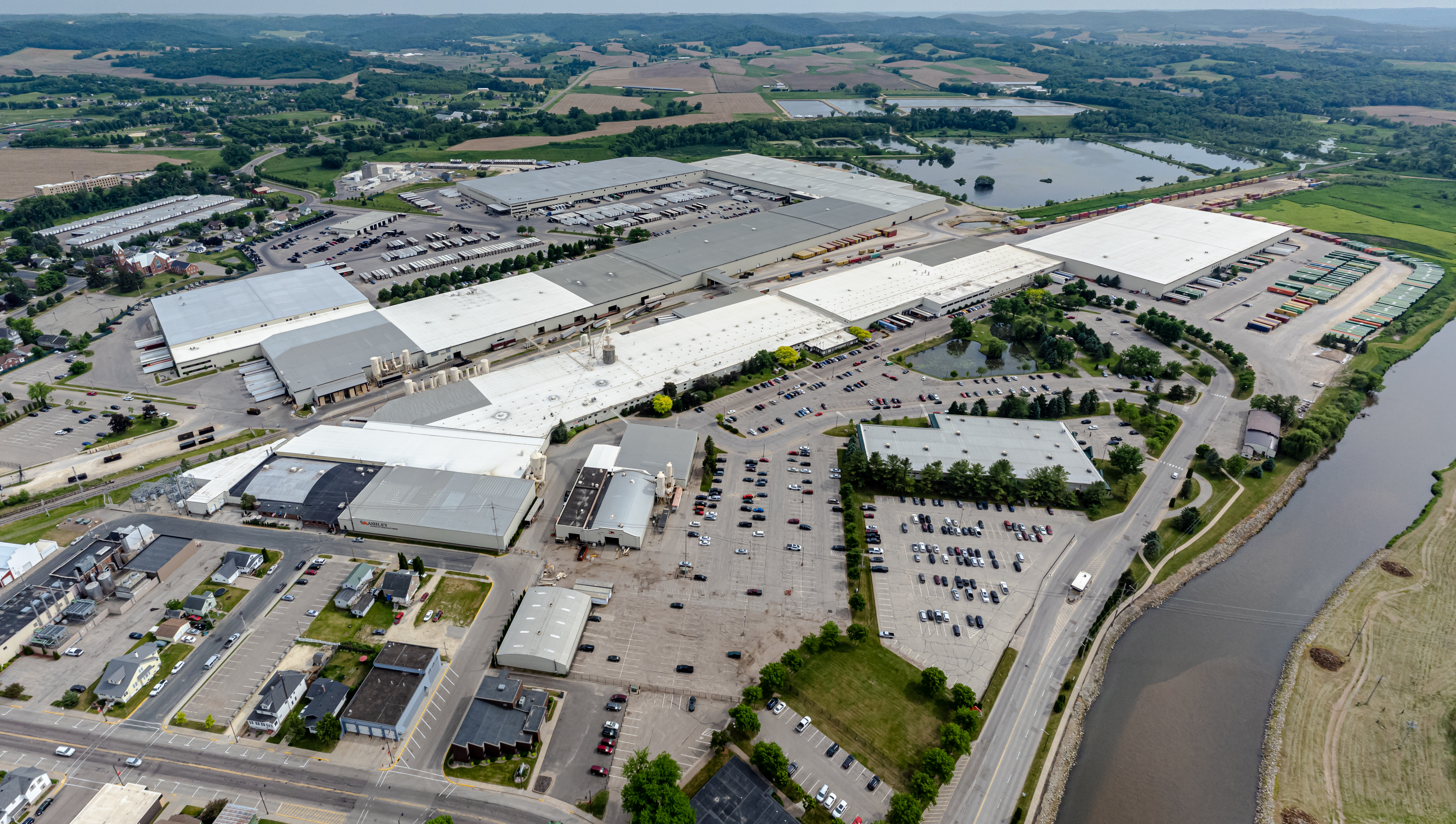 Aerial panoramic view of a large industrial warehouse complex with parking lots and a waterway.