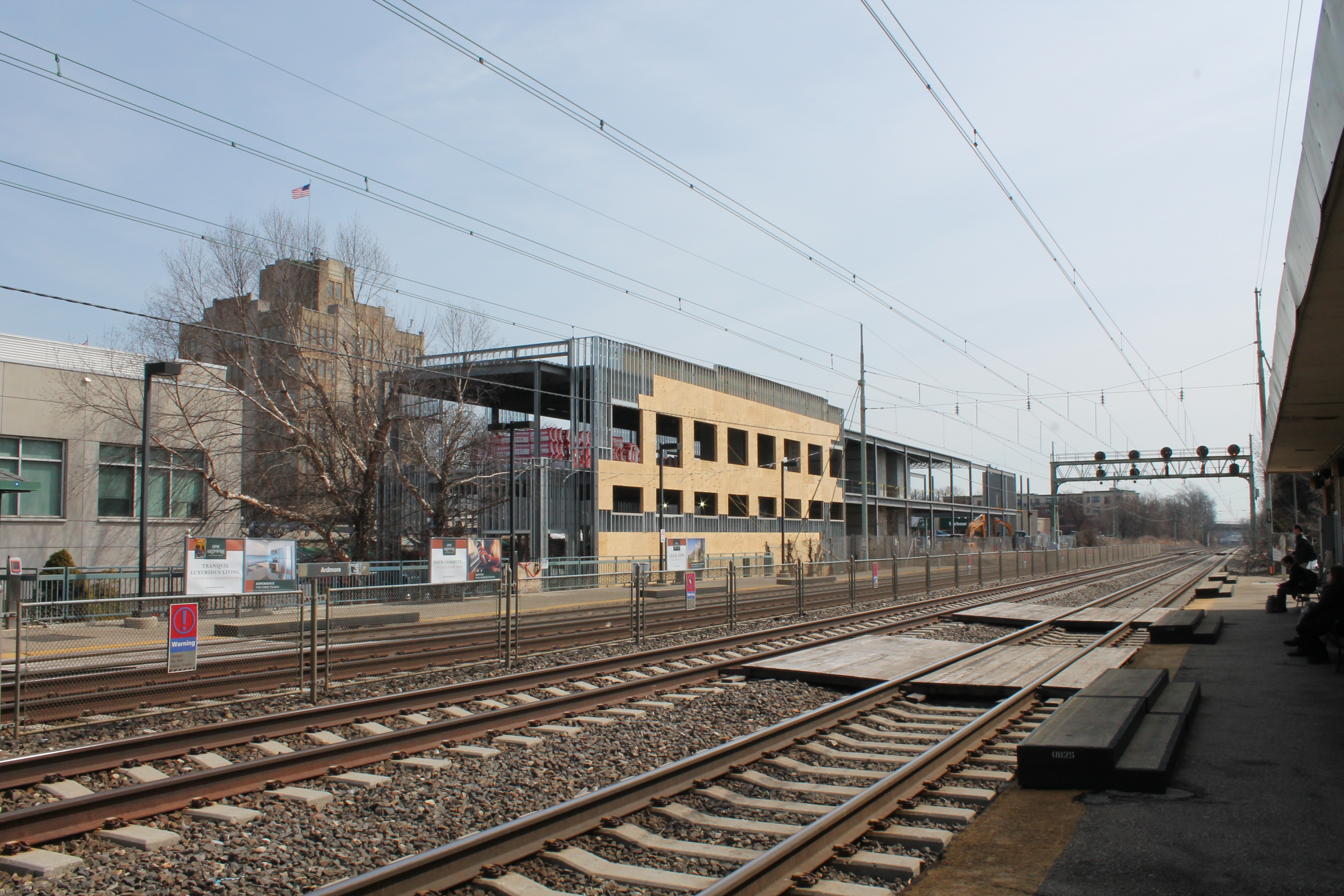 Steel-framed building under construction beside a commuter rail platform.