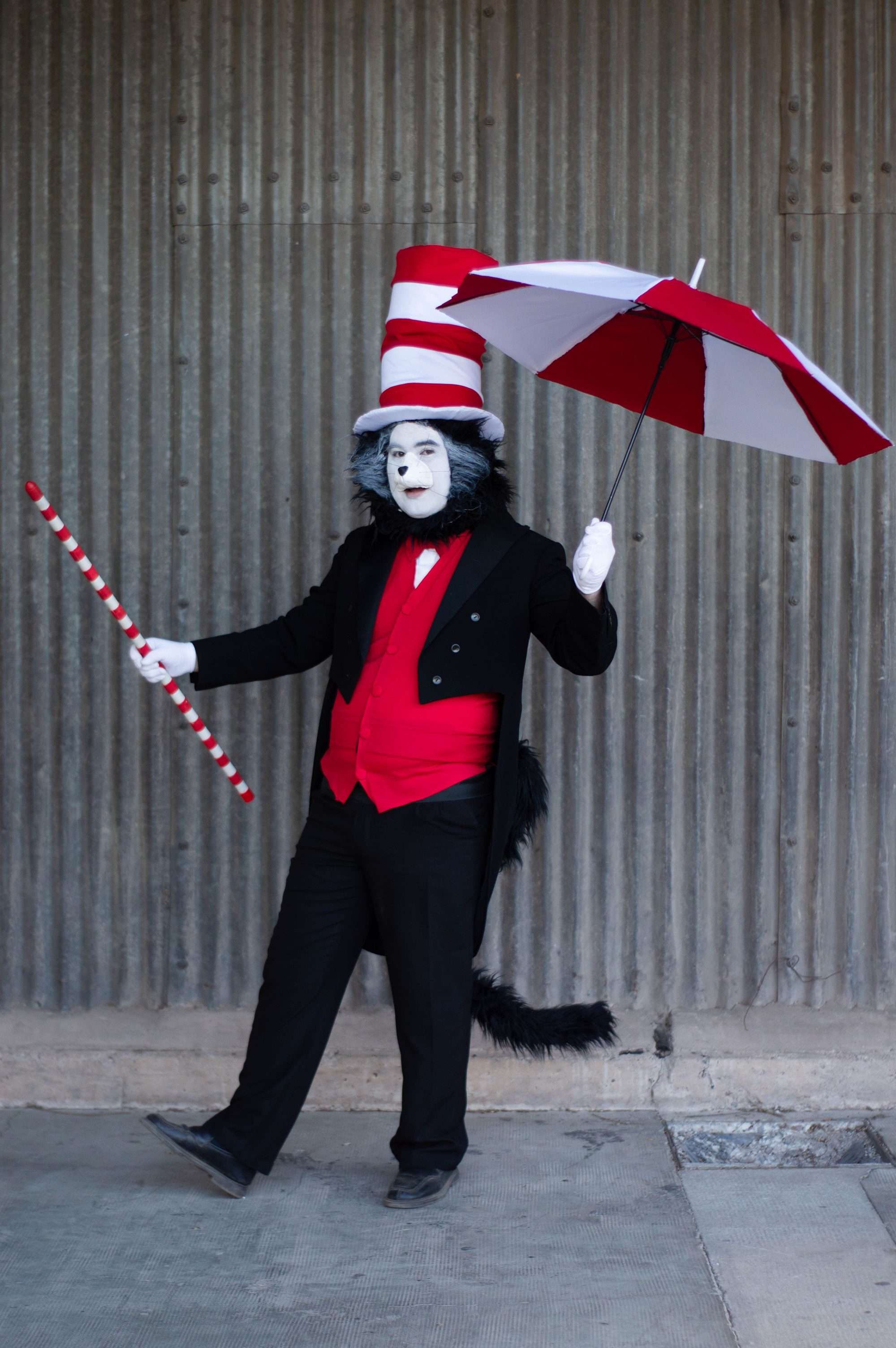 Person in Cat in the Hat costume with umbrella and staff against a concrete background.