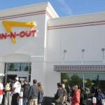 Crowd of people lined up outside an In-N-Out Burger restaurant with red and yellow signage.