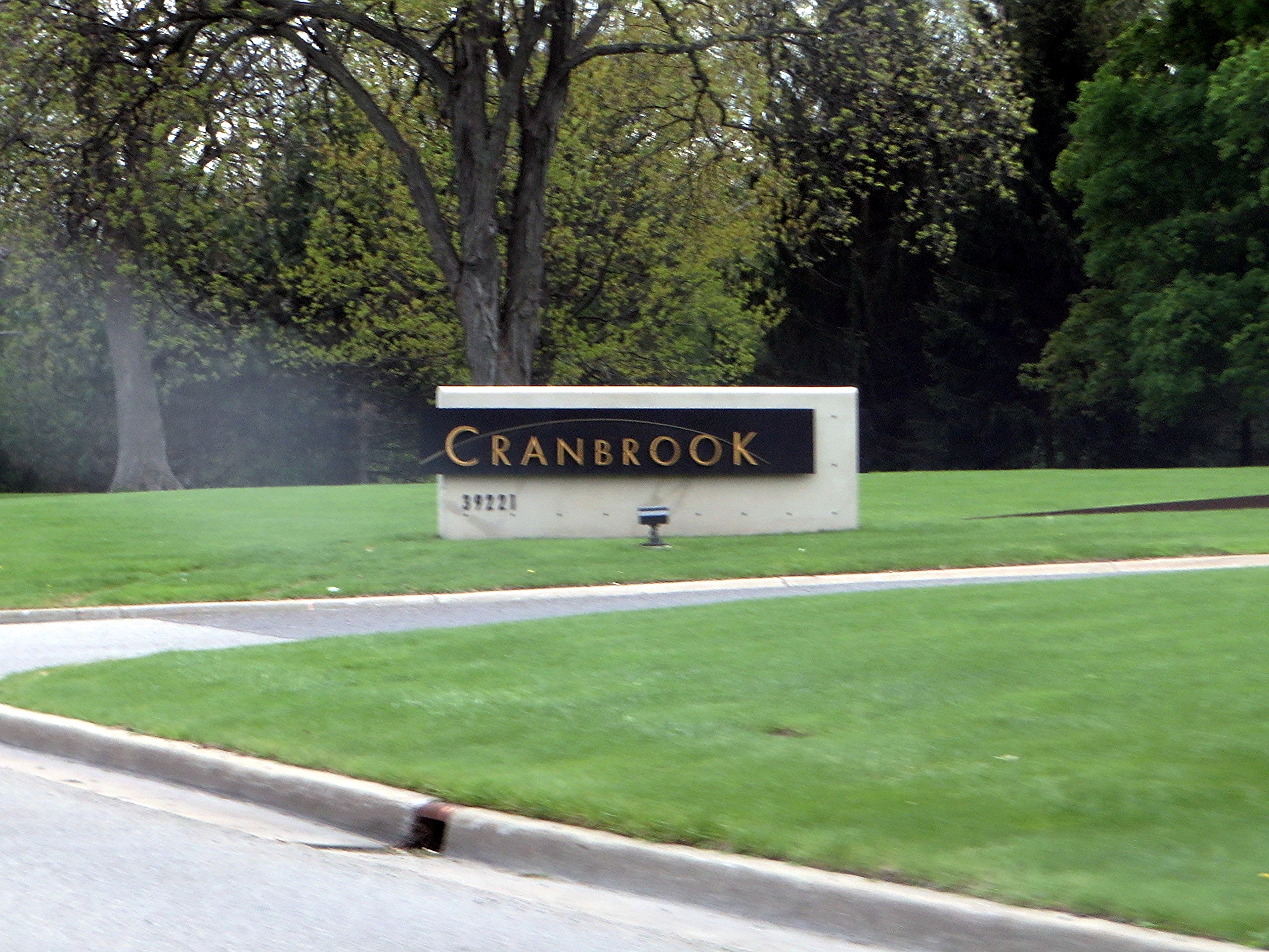 Stone entrance sign reading 'Cranbrook' set against a green lawn and trees.