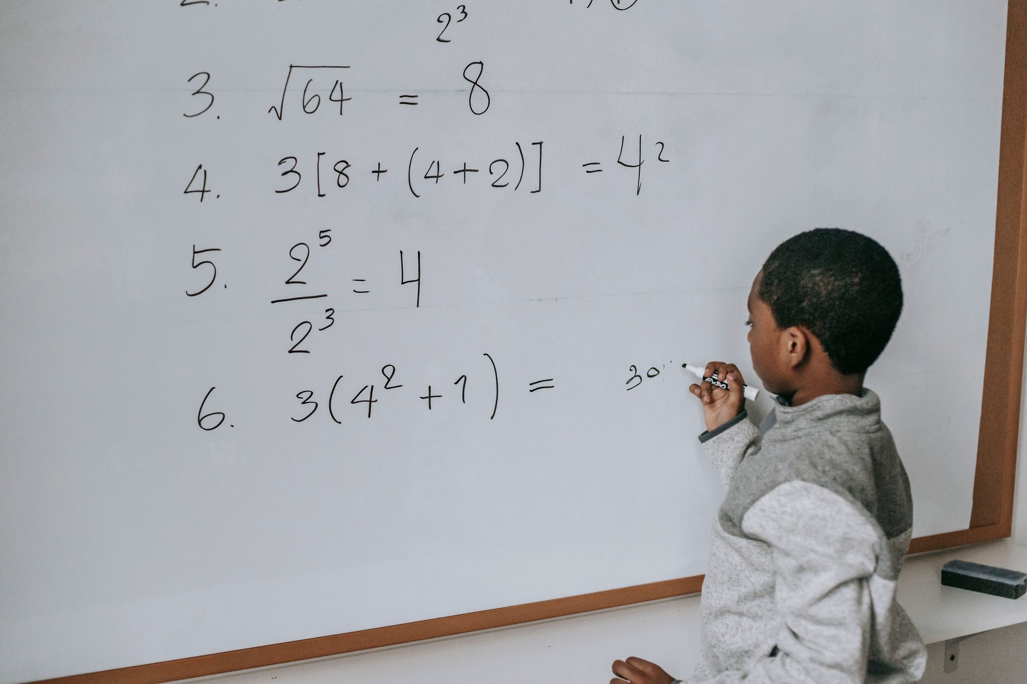 Side view of a student standing near whiteboard in classroom and solving math examples during lesson at school.