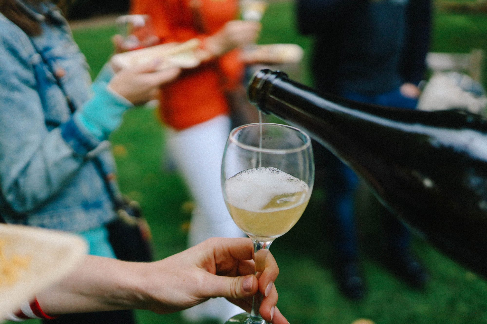 A close-up of wine being poured into a glass during a casual outdoor gathering.