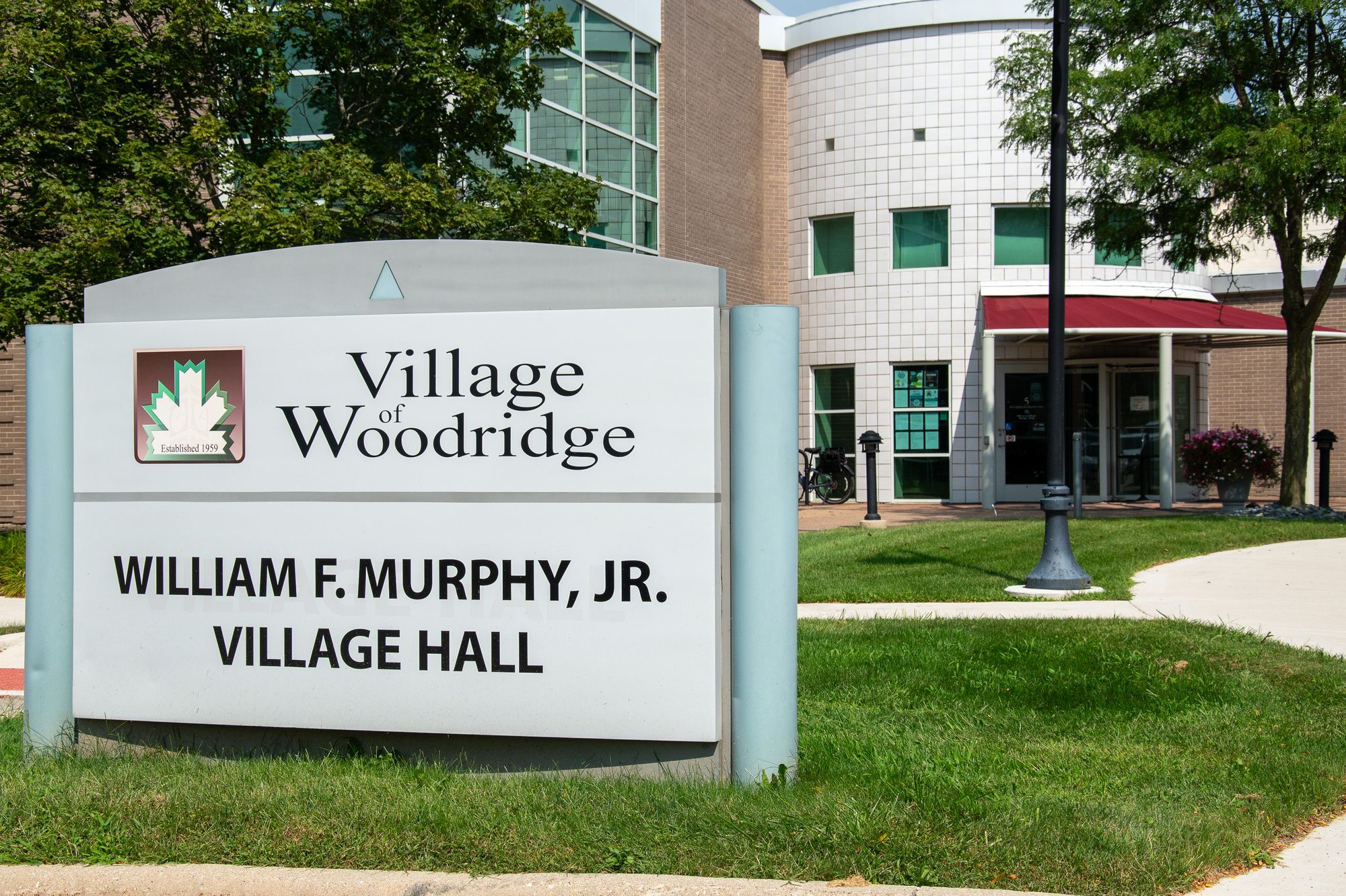 Exterior sign and entrance of a modern brick-and-glass village hall building.