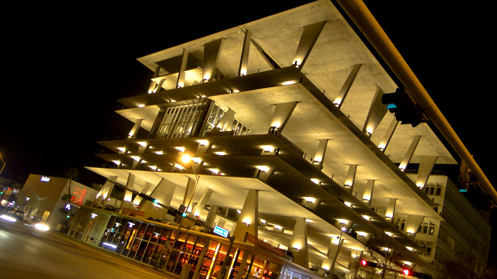 Multi-story parking garage lit up at night with cantilevered concrete floors.