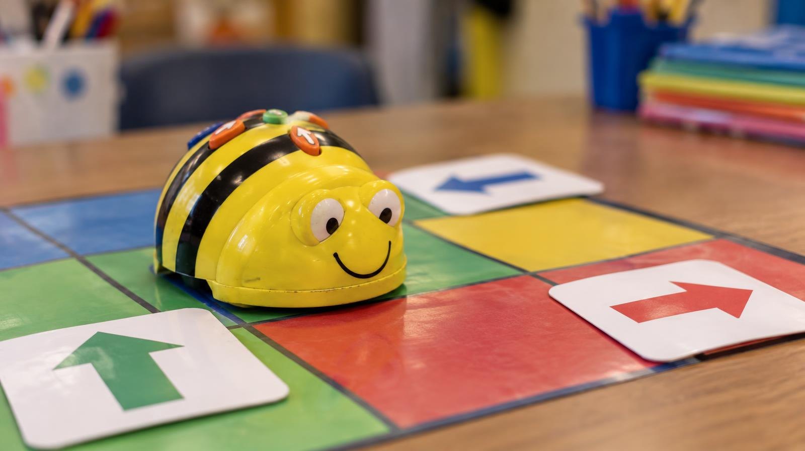A small colorful programmable robot on a bright grid mat with arrow cards.